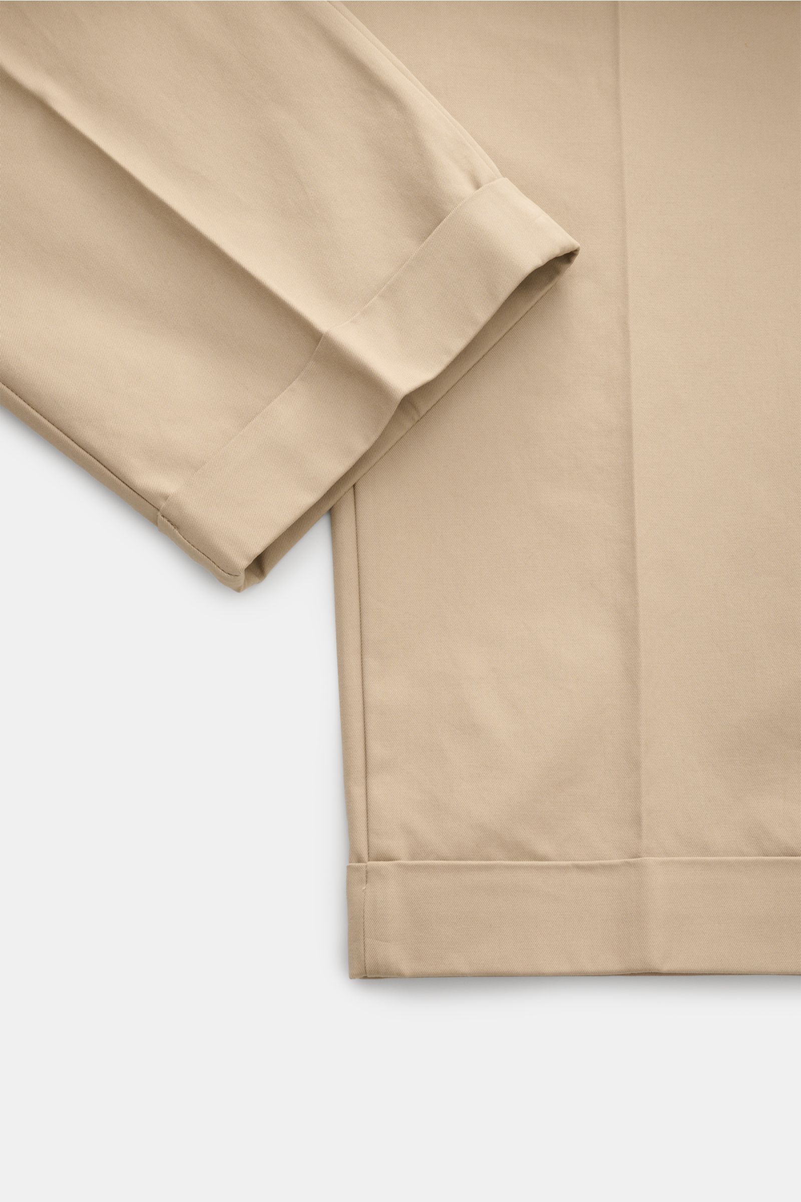A close-up top-down view of the Ami Paris Baumwollhose beige showing the folded hem and smooth cotton fabric, featuring reine Baumwolle, glatter Griff, Tapered Fit, reguläre Oberschenkelweite, knöchellang, Button Fly und Bundknopf, Gesäßtaschen mit Knopf,