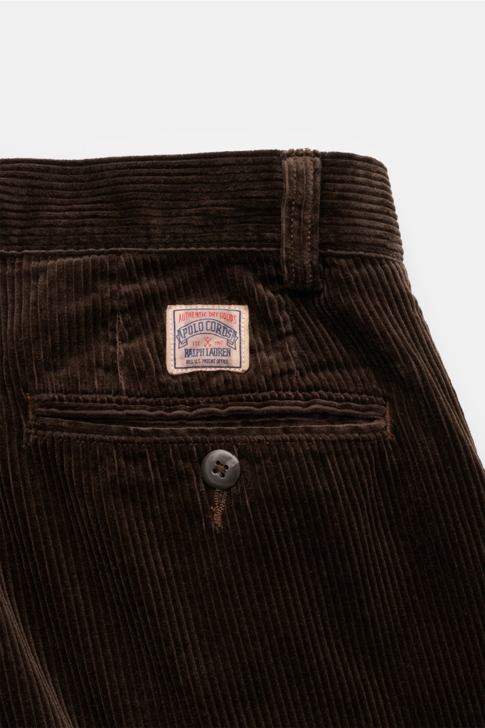 Polo Ralph Lauren Cordhose dunkelbraun aus Baumwoll-Cord mit Bundfalten, kleiner Uhrentasche, französischen Taschen, Knopf-Detail, von hinten nah fotografiert.