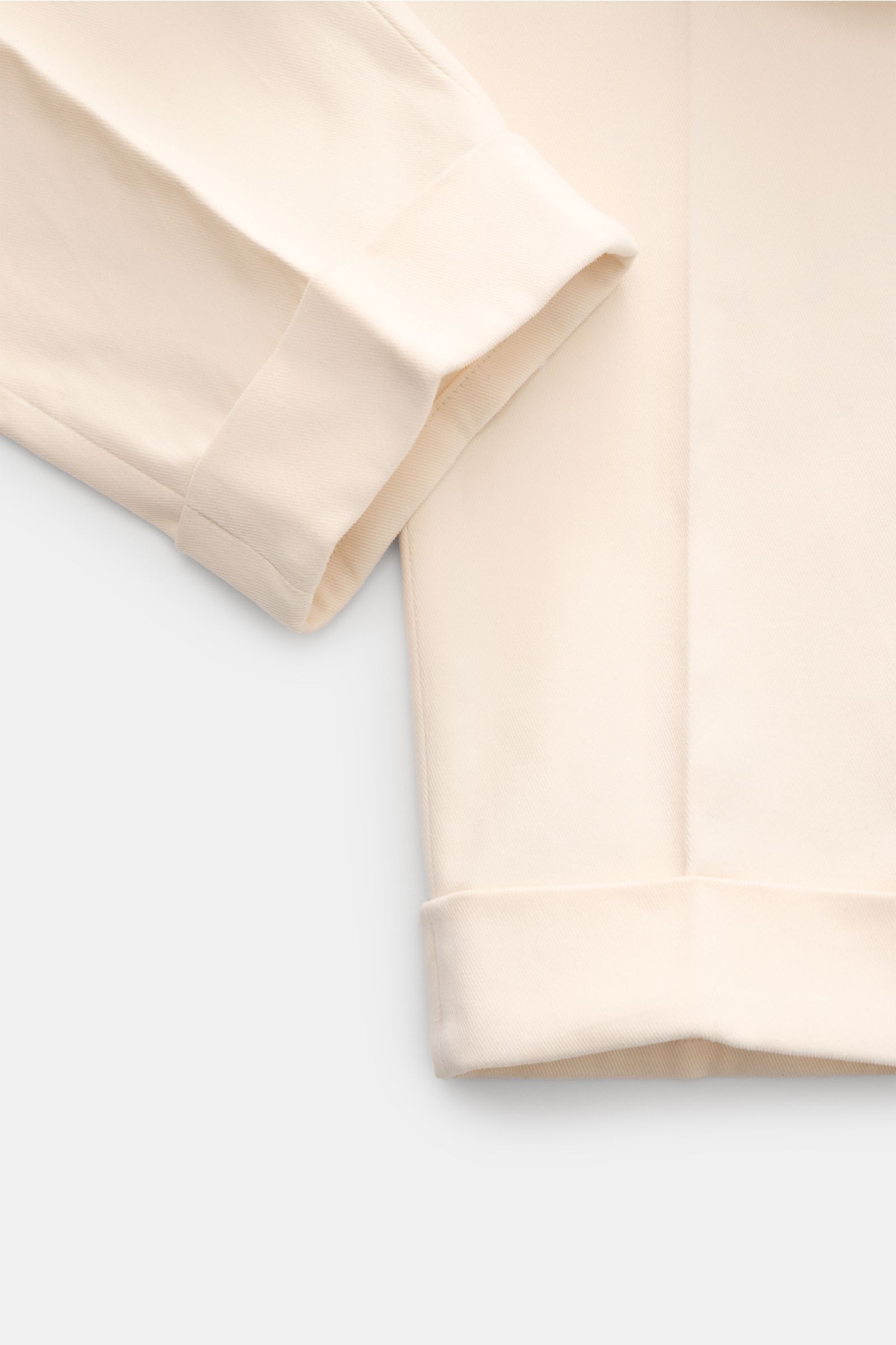 Close-up front view of the lower leg section of the PT Torino Chino 'Carrot Fit' creme, showing the soft twill cotton fabric with a slightly elastic quality, a fixed hem cuff, and detailed double pleats with a stylish extended button fly. The chino featur