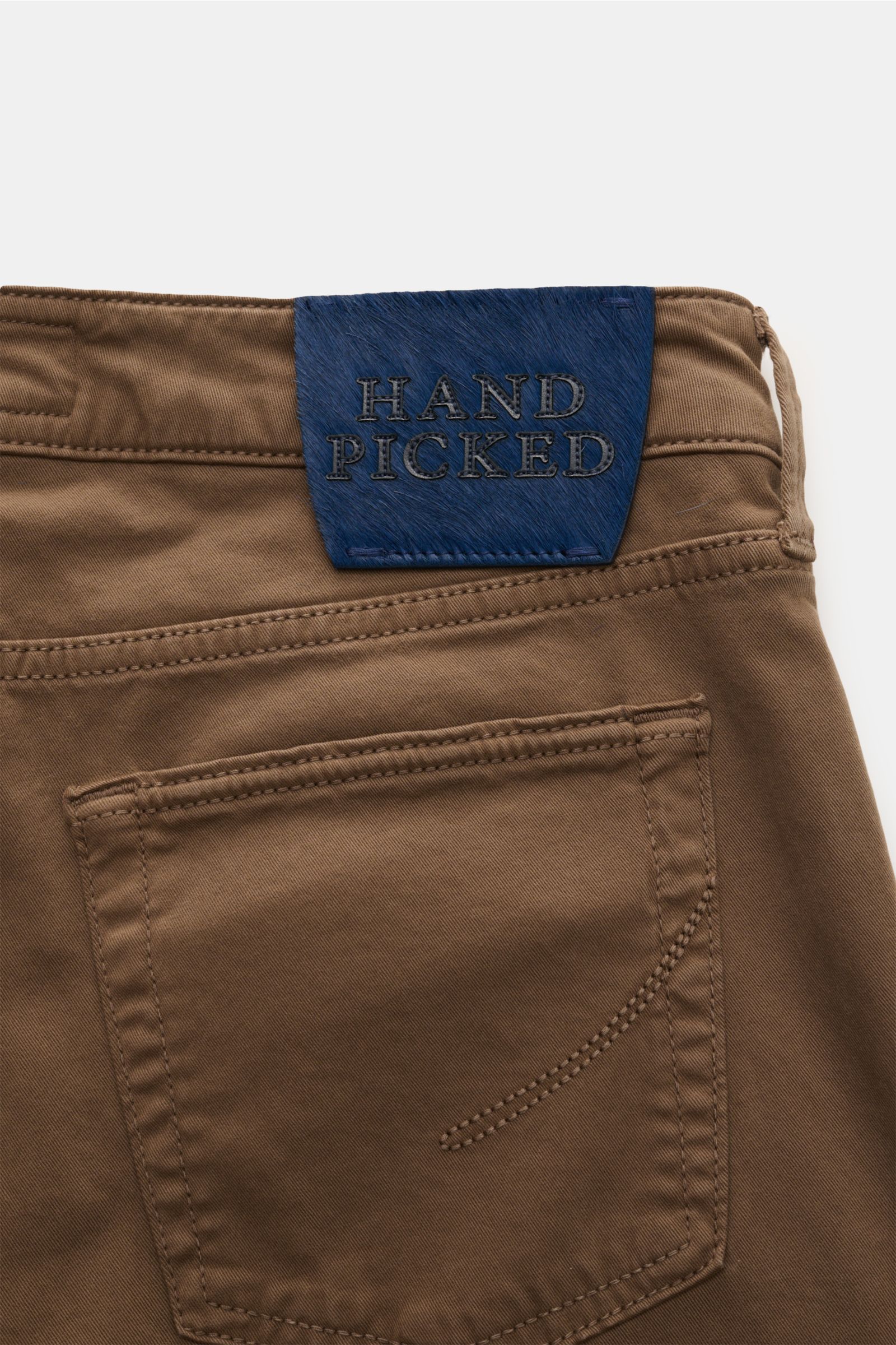 Close-up rear view of HandPicked Chinos 'Parma' brown in cotton twill with slightly elasticated fabric, soft feel, slim fit, very tapered cut, button fly, French pockets, coin pocket with initial, back pockets with stitching, and a blue leather patch in p