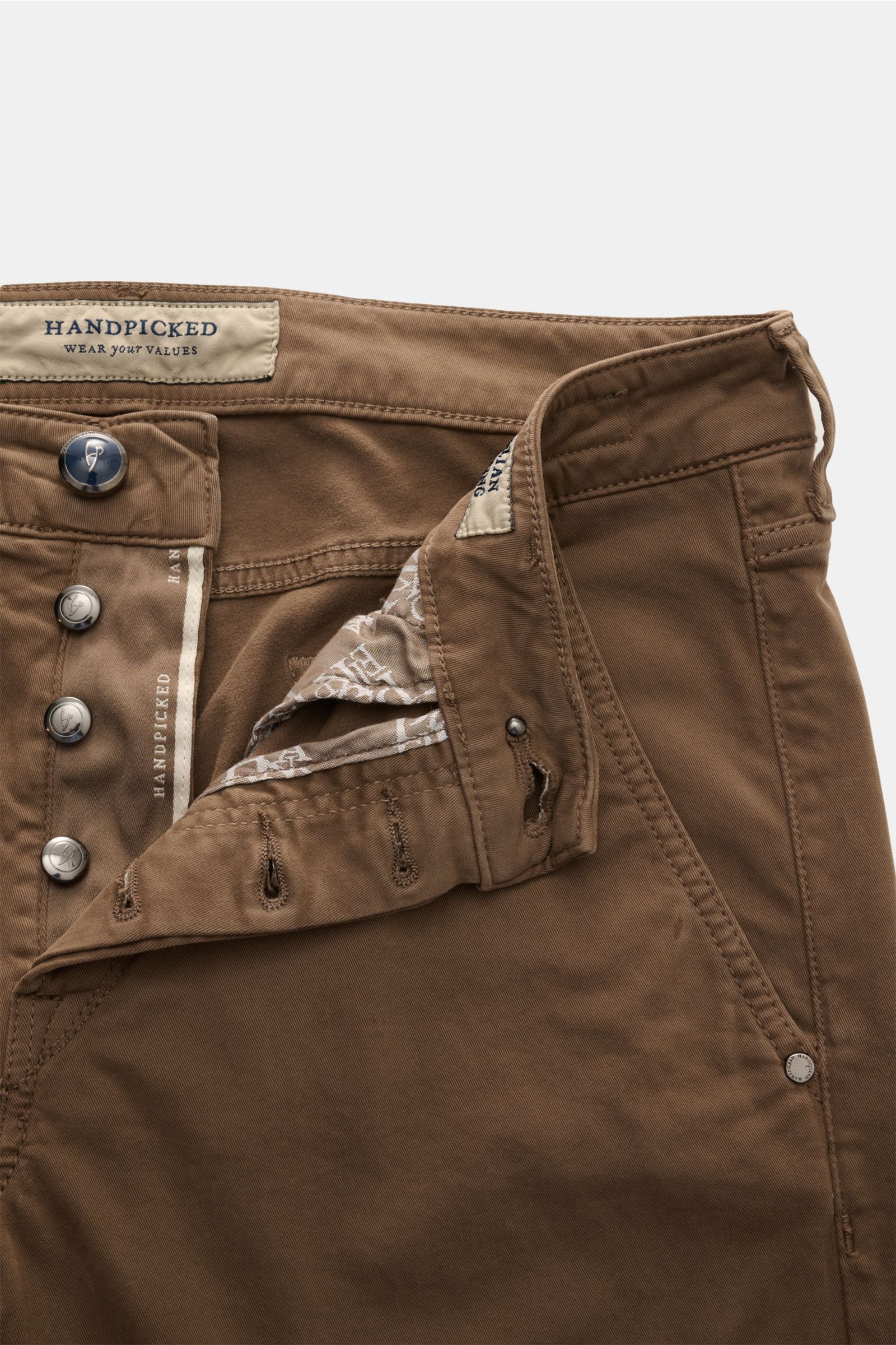 Close-up from above of the HandPicked Chinos 'Parma' brown showing cotton twill, slightly elasticated fabric, soft feel, slim fit, very tapered cut, button fly, French pockets, coin pocket with initial, back pockets with stitching, and a leather patch in 