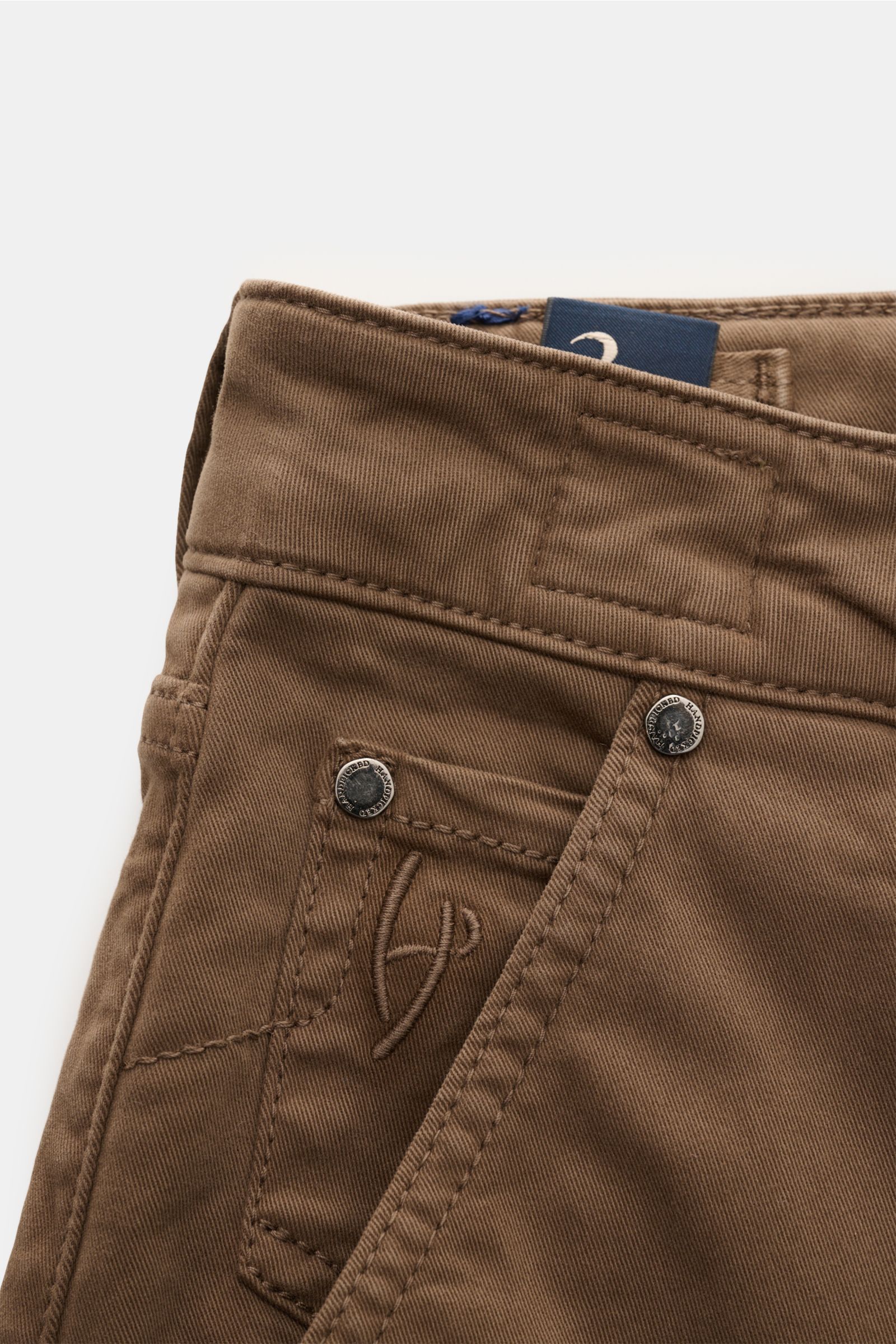 Close-up front-angle view of HandPicked Chinos 'Parma' brown showcasing cotton twill, slightly elasticated soft fabric, slim fit, very tapered cut, button fly, French pockets, coin pocket with initial, back pockets with stitching, and leather patch in pon