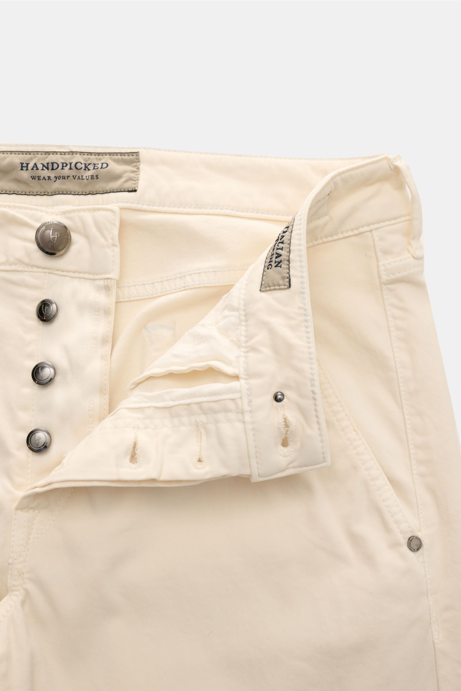 HandPicked Chinos 'Parma' cream shown from front close-up, featuring cotton twill, slightly elasticated fabric, soft feel, slim fit, very tapered cut, button fly, French pockets, coin pocket with initial, back pockets with stitching, and leather patch in 
