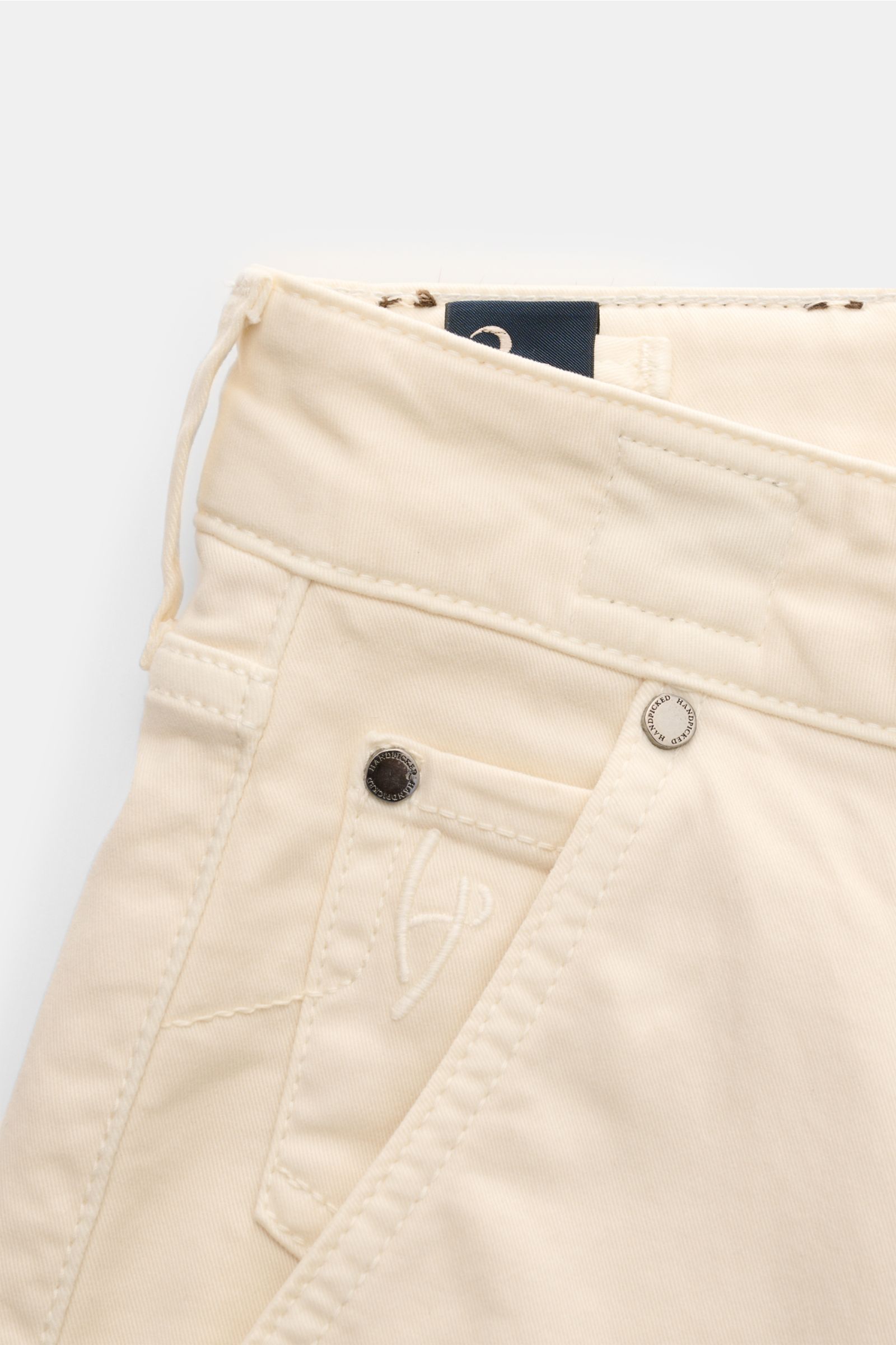 Close-up front view of HandPicked Chinos 'Parma' cream made of cotton twill, slightly elasticated fabric with a soft feel, slim fit, very tapered cut, button fly, French pockets, coin pocket with initial, back pockets with stitching, and leather patch in 