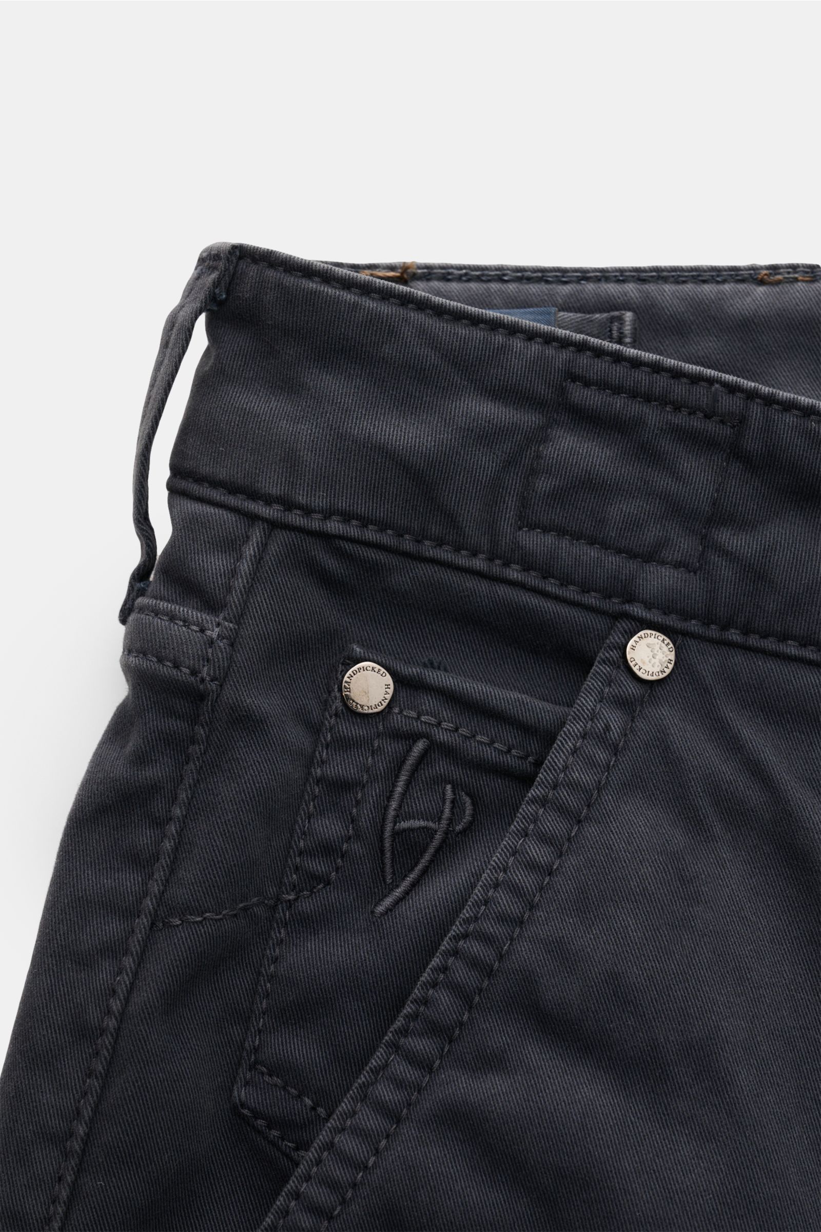 Close-up front angle of HandPicked Chinos 'Parma' anthracite showing cotton twill, slightly elasticated fabric, soft feel, slim fit, very tapered cut, button fly, French pockets, coin pocket with initial, back pockets with stitching, and leather patch in 