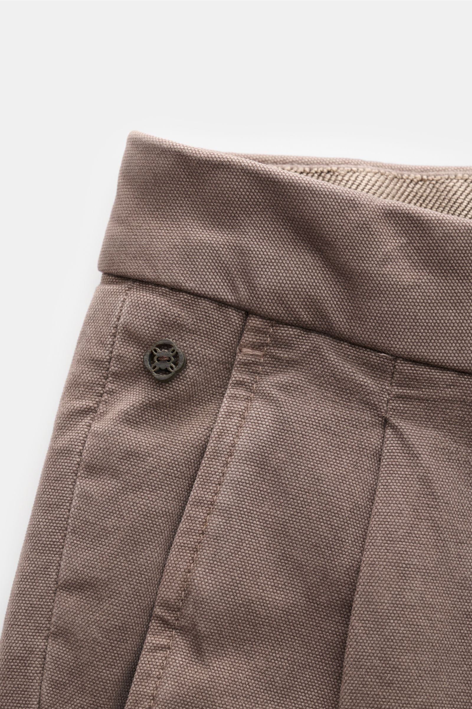 Close-up front-side view of GTA Hose 'Luca' taupe showcasing the high-quality cotton-modal mix fabric with a soft, slightly elastic texture, tapered fit, double waistband pleat, fixed hem cuff, and small logo detail. Die Hose 'Luca' von GTA überzeugt a