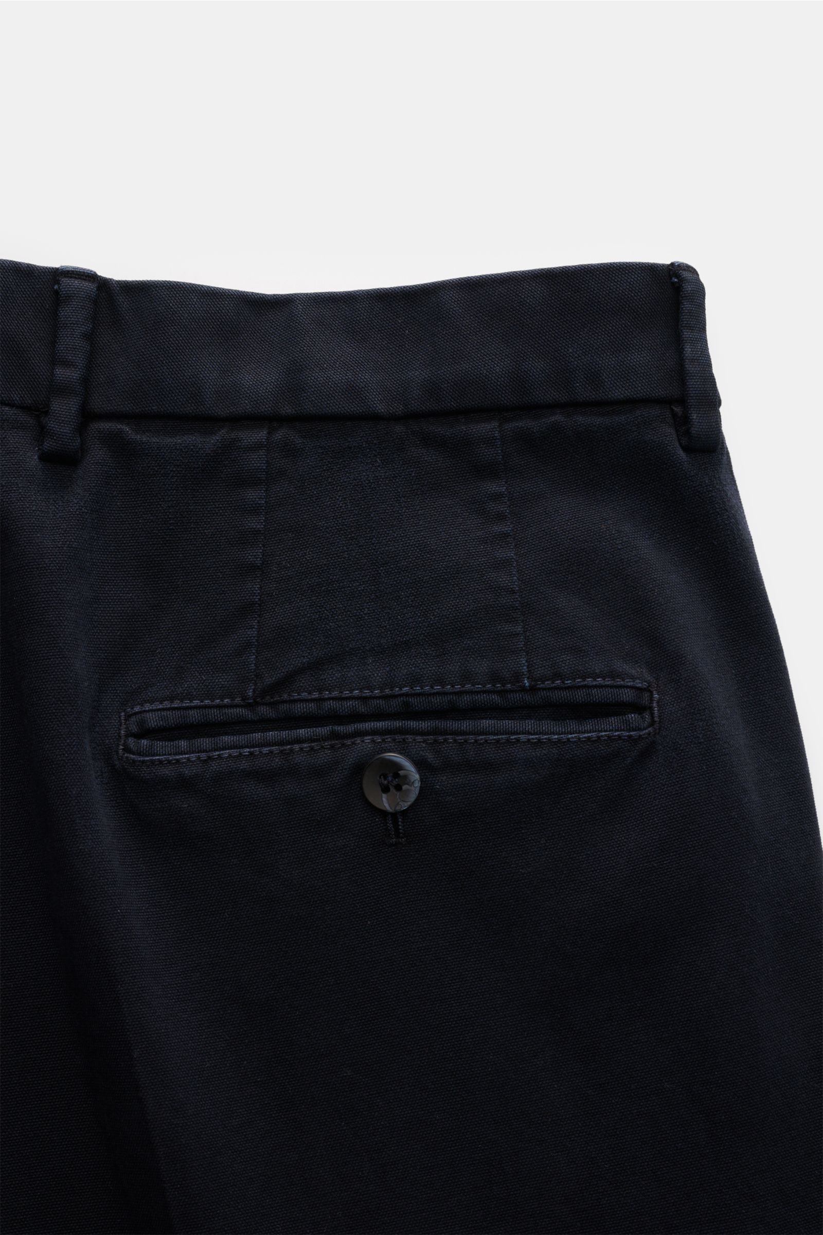 Close-up rear view of the GTA Hose 'Luca' navy showcasing the garment dyed, soft cotton-modal blend with a single buttoned back pocket and belt loops. The tapered fit features double pleats, an elastic waistband insert, French pockets, and a fixed hem cuf