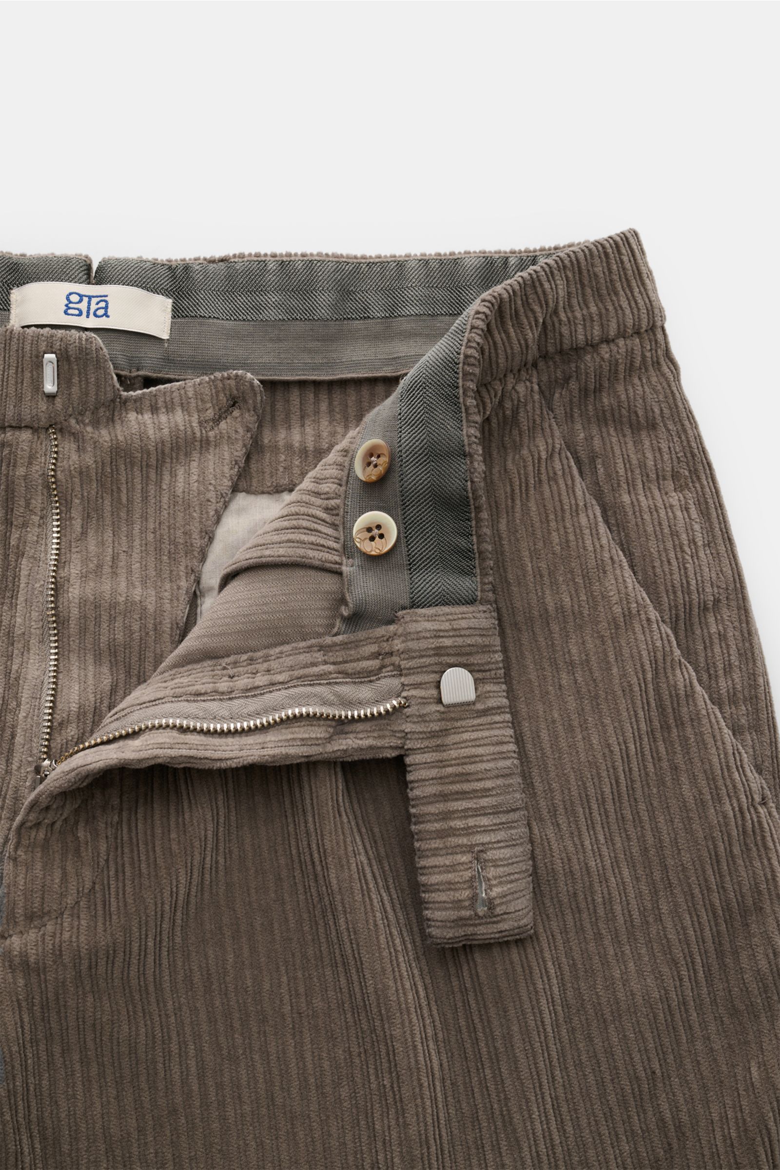 Close-up front view of the GTA Cordhose 'Silvio' taupe, showing cord cotton fabric, slightly elastic quality, soft touch, regular fit, tapered cut, zipper and button closure, elastic waistband insert, single pleat, French pockets, and welt pockets at the 