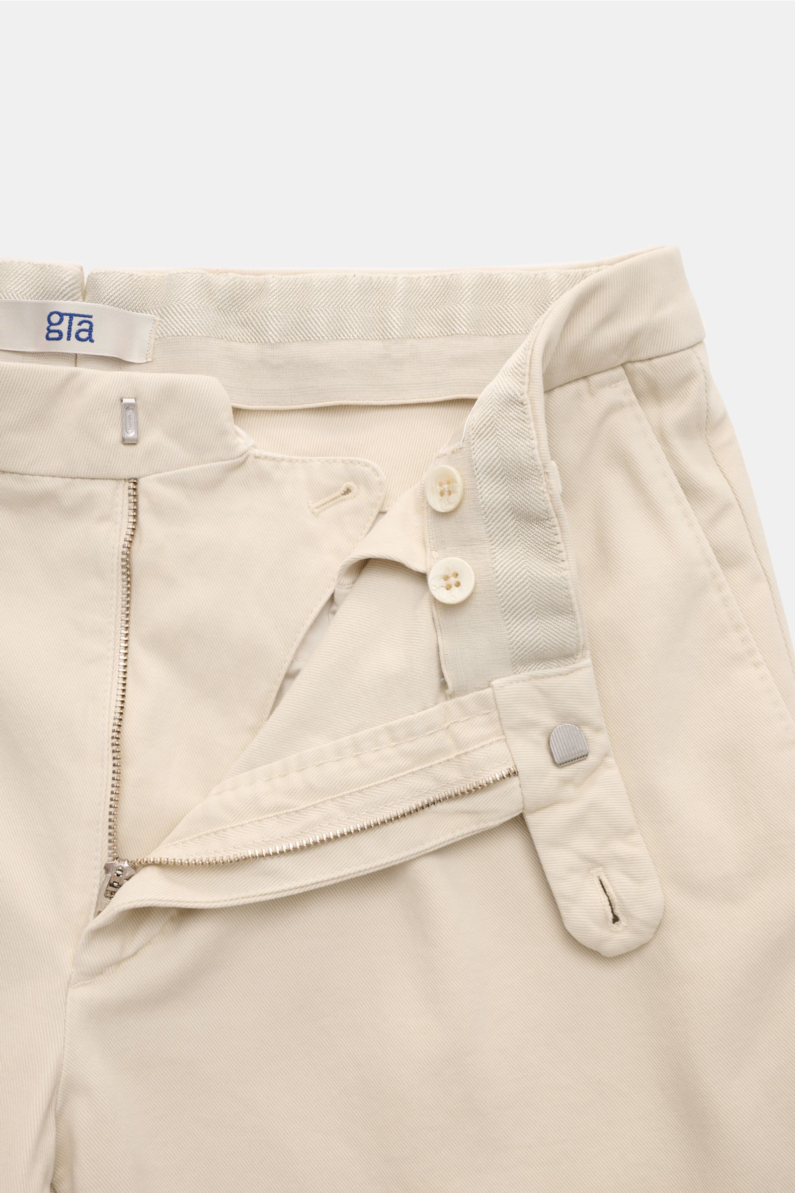 GTA Chino 'Federico' sand aus Twill mit Cashmere-Anteil, Regular Fit, schmal zulaufend, Reißverschluss, Bundknopf, elastischer Bund, französische Taschen, paspelierte Gesäßtaschen mit Knopf, Aufnahme von oben auf den geöffneten Bund.