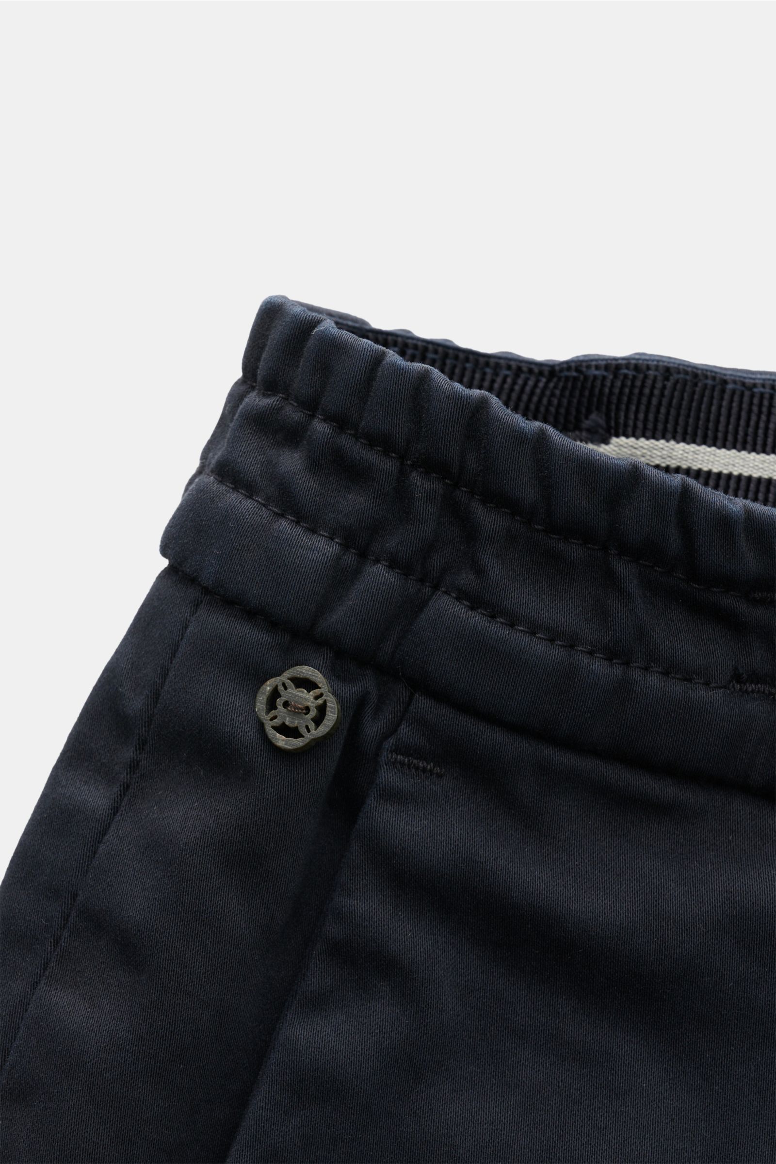 Close-up top-down view of the elasticated waistband and small logo detail on navy GTA Cotton trousers 'Dennis'. The cotton trousers 'Dennis' by GTA are defined by their soft feel and feature an elasticated waistband for comfort. Slightly elasticated cotto