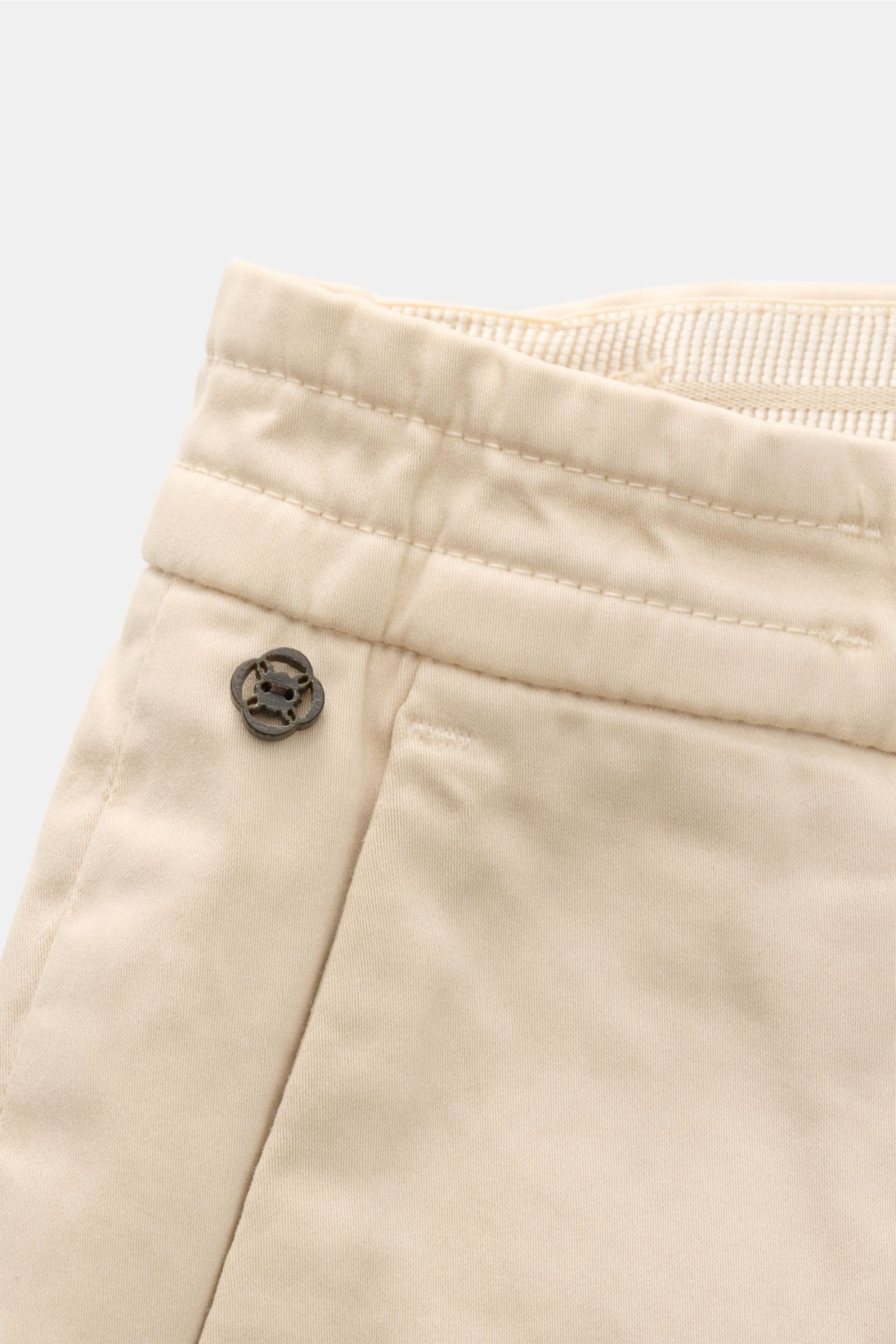 Close-up front view of GTA Cotton trousers 'Dennis' sand, showing soft, slightly elasticated cotton fabric, partially elasticated waistband, small logo detail, and fine stitching. The cotton trousers 'Dennis' by GTA are defined by their soft feel and feat