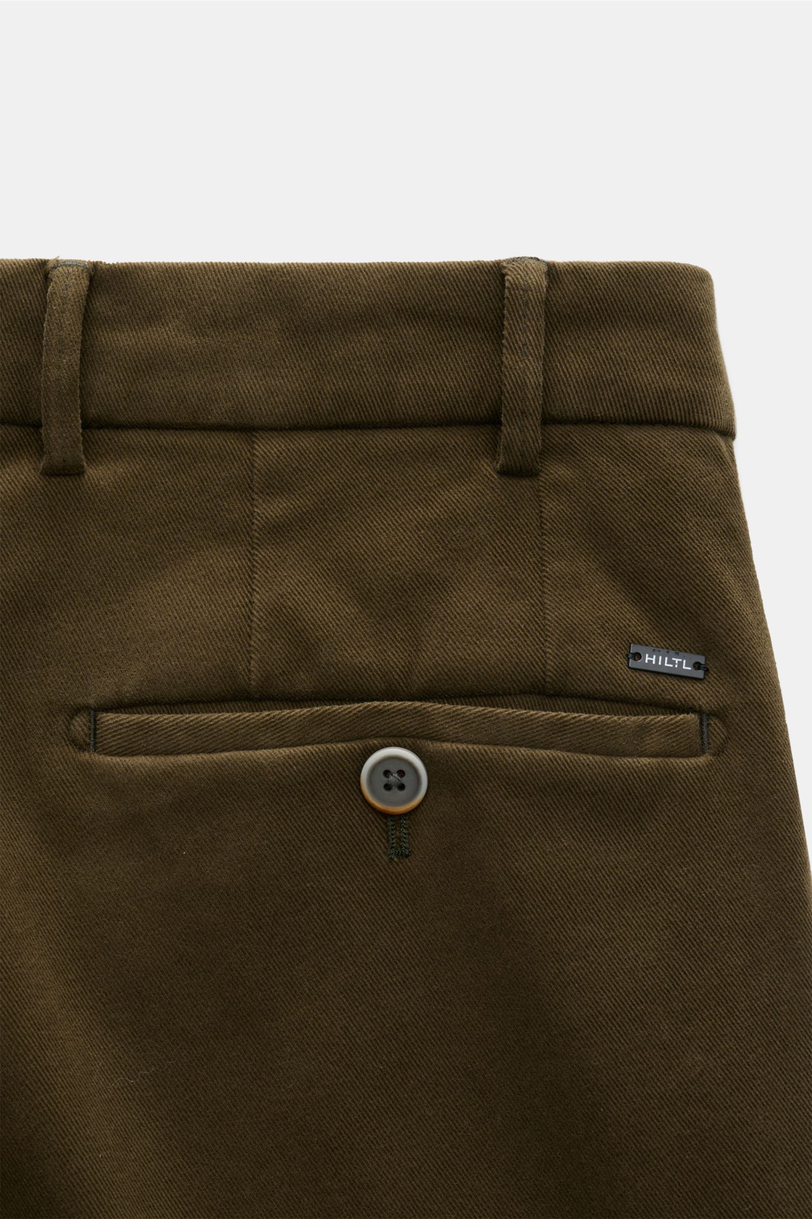 Hiltl Baumwollhose 'Parma' dark olive, schmal zulaufend, Slim Fit, elastische Baumwolle, Detailaufnahme der paspelierten Gesäßtasche mit Knopf und Logo, von hinten.