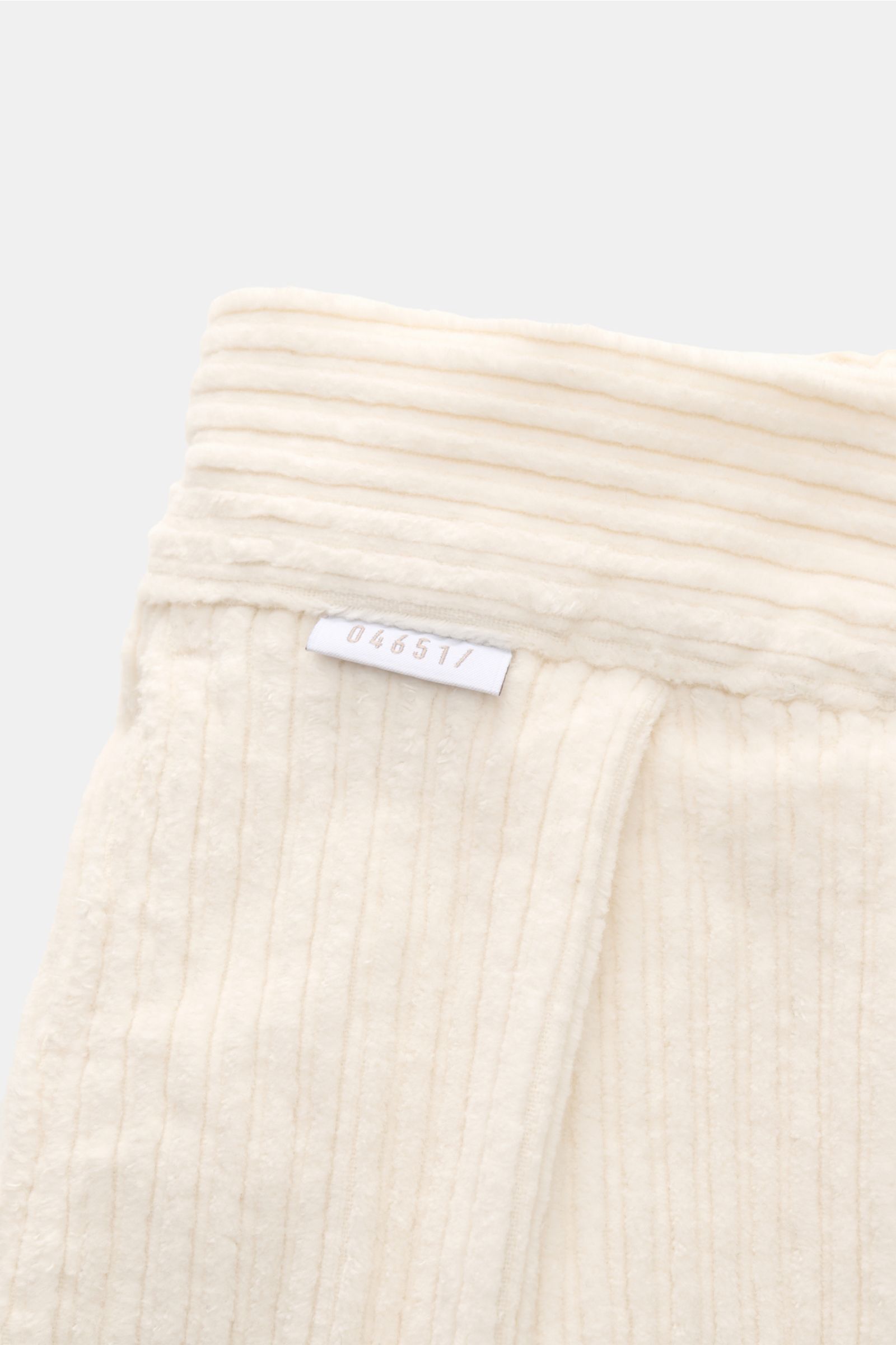 Hochauflösende Nahaufnahme der cremefarbenen 04651/ A trip in a bag Cordhose creme aus Baumwoll-Cord mit doppelter Bundfalte, kleinem Weblabel, weichem Griff und feiner Rippstruktur, fotografiert von oben.