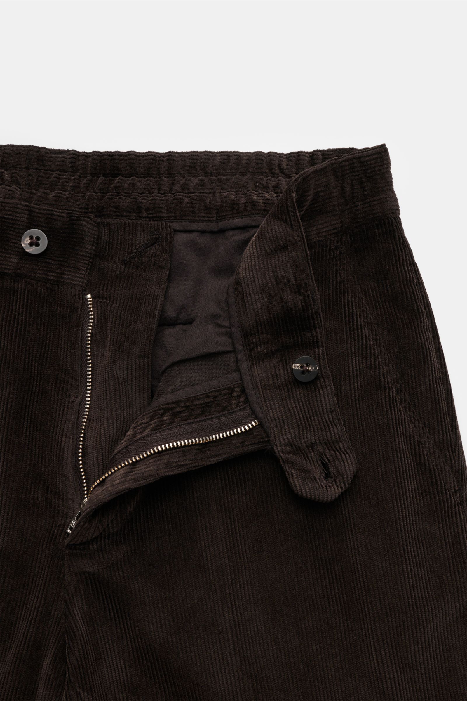 Close-up front view of 04651/ A trip in a bag Cordhose dunkelbraun, garment dyed dark brown cotton-modal corduroy pants with partially elastic waistband, zipper, button, and smart pockets. Welcome to the Autumn Winter Collection by 04651/ A TRIP IN A BAG 