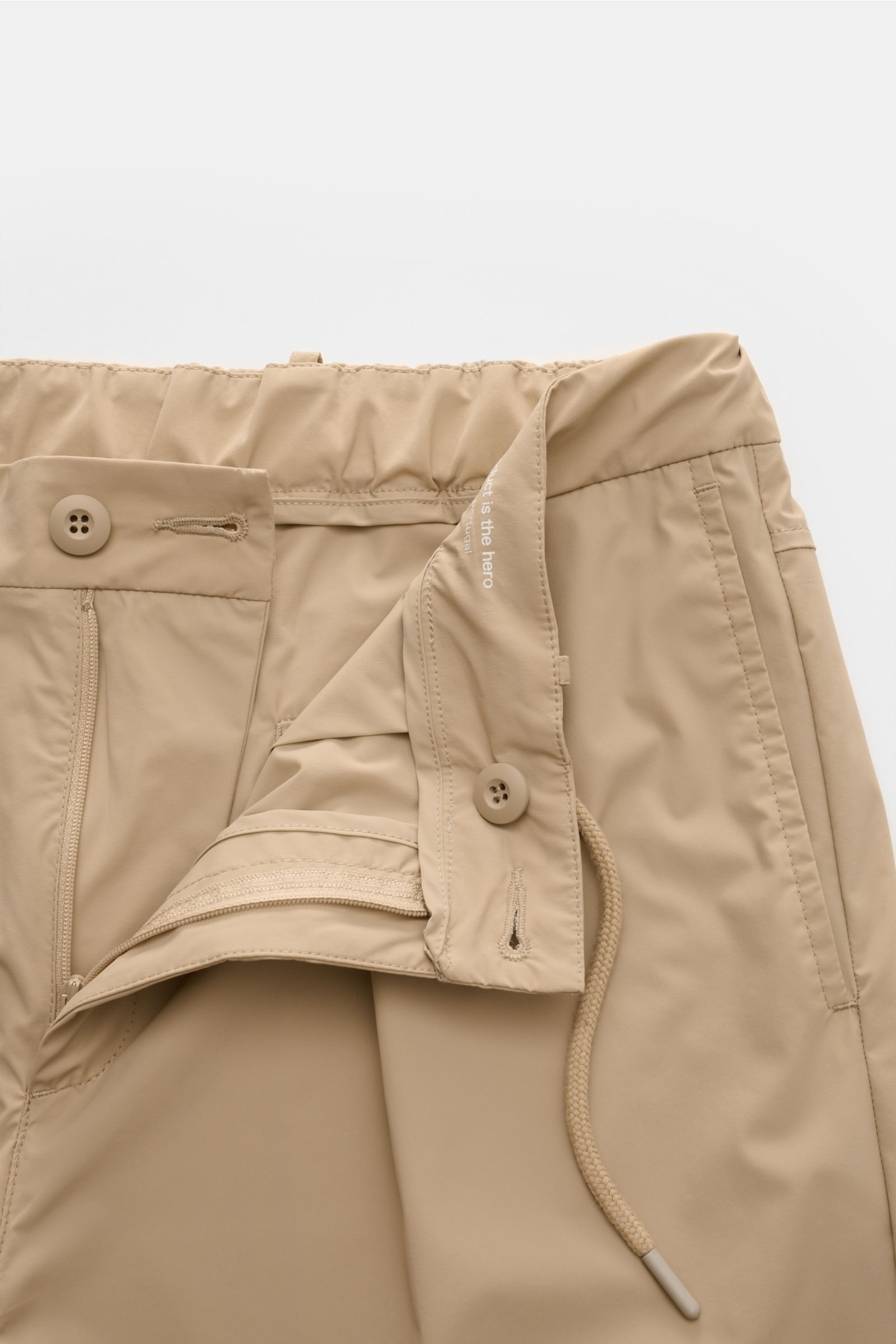 The Product is the Hero Jogpants beige, Nahaufnahme der Bundöffnung aus schräger Perspektive, hochwertige Microfaser, glatter Griff, tapered fit, reguläre Oberschenkelweite, knöchellang, sehr schmal zulaufend, teilelastischer Bund mit Tunnelzug, französis