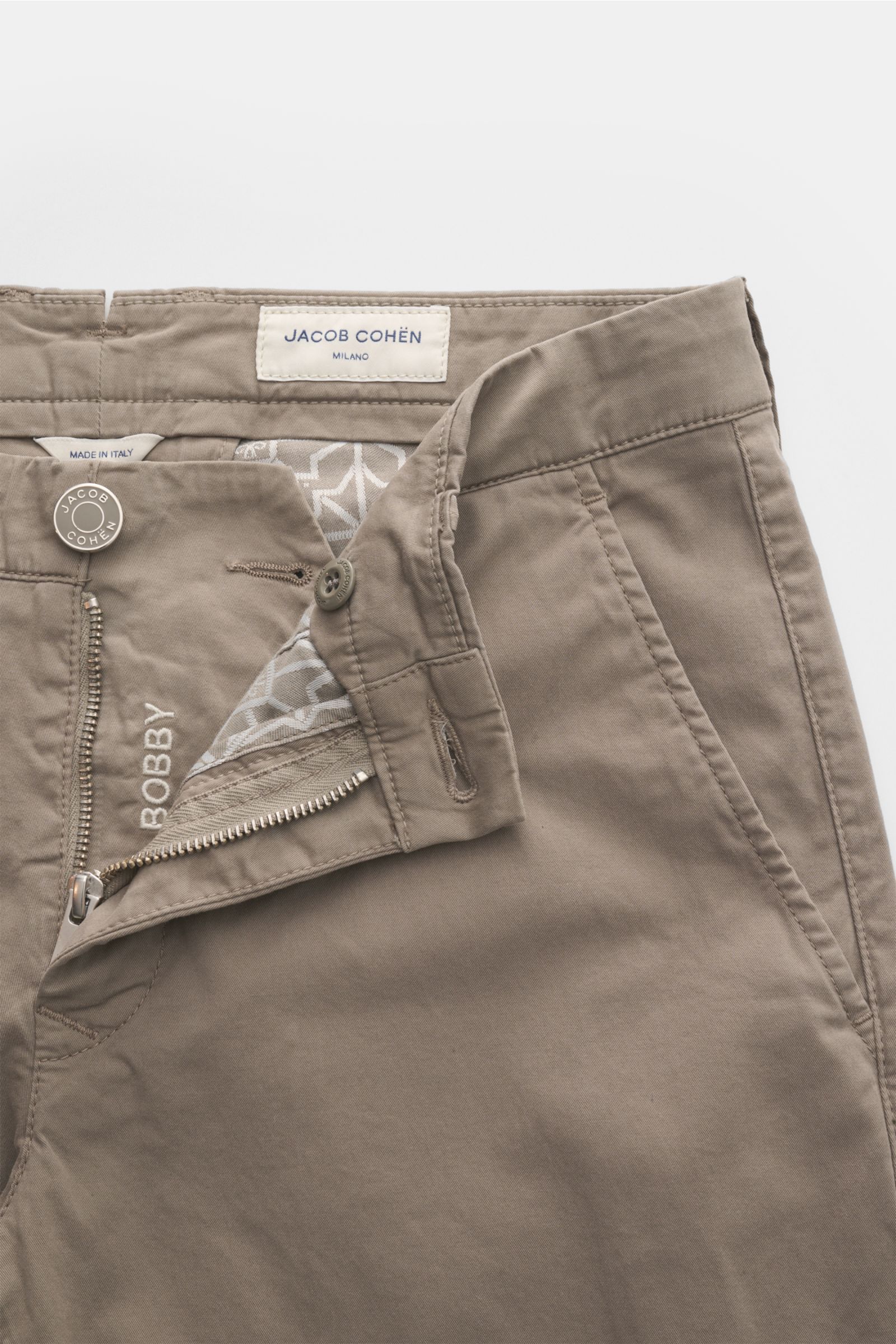 Jacob Cohen Chino 'Bobby' taupe shown from a top-front perspective with open zipper and button, featuring fine cotton twill, stretch, slim fit, low waist, French pockets, coin pocket, back pockets with buttons, garment dyed, soft touch, and velour leather