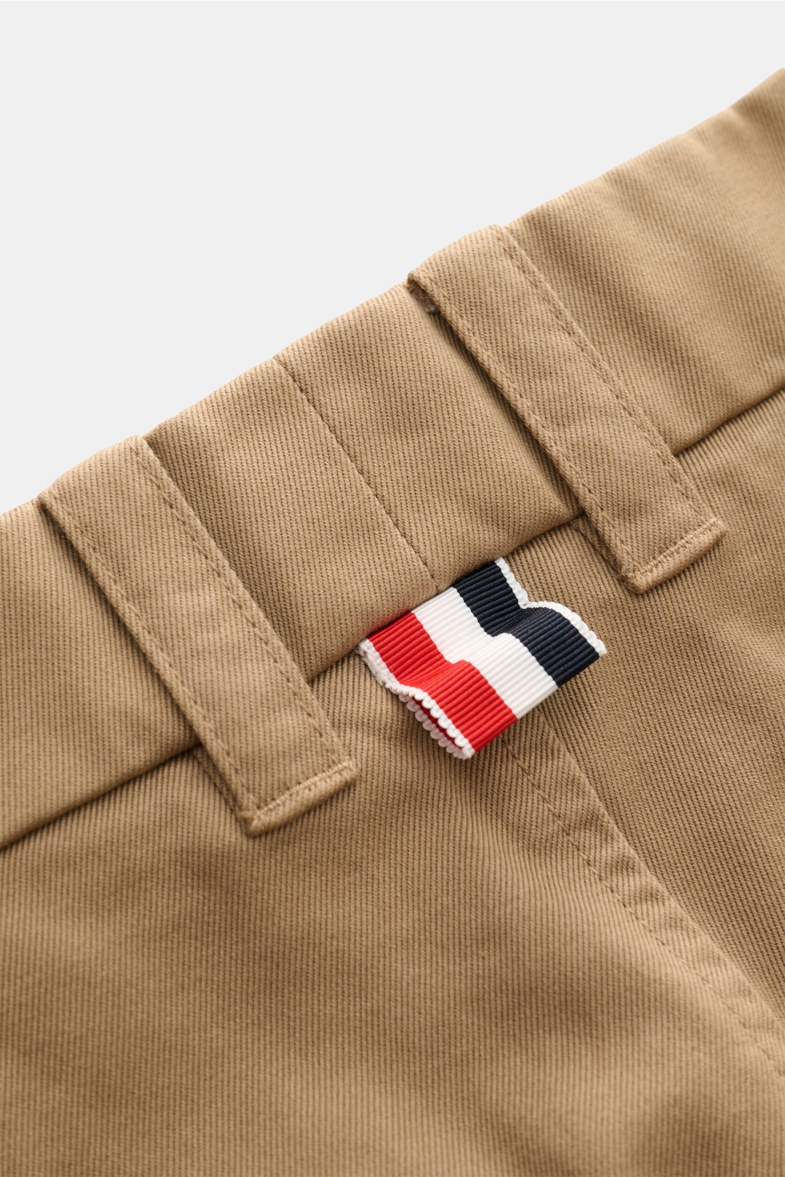 Nahaufnahme der hellbraunen Thom Browne Chino mit Tapered Fit, Baumwoll-Twill, Bundschlaufen und markantem Flaggen-Label.