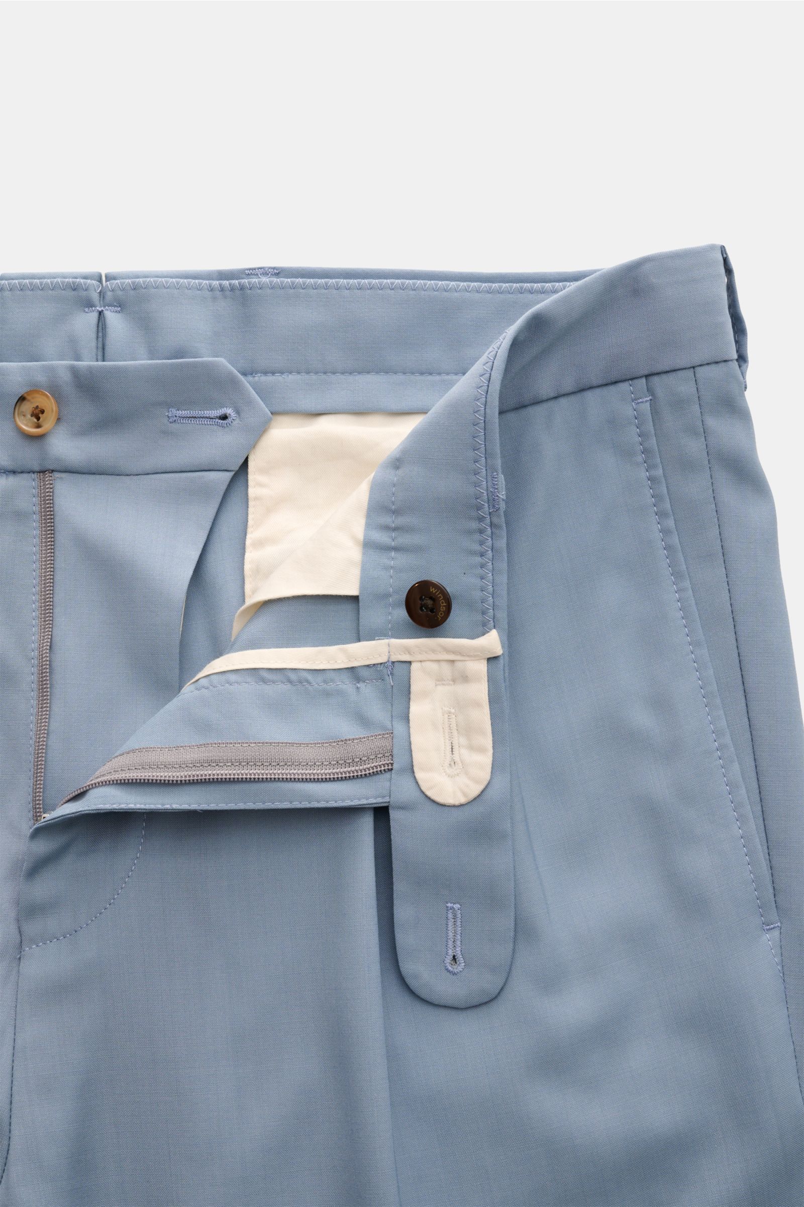 Close-up front view of Windsor Wool trousers 'Sapo' smoky blue showing zip, waist buttons, and inner lining in pure wool with smooth feel, tapered fit, regular thigh width, ankle length, French pockets, small watch pocket with flap, double pleat, back poc