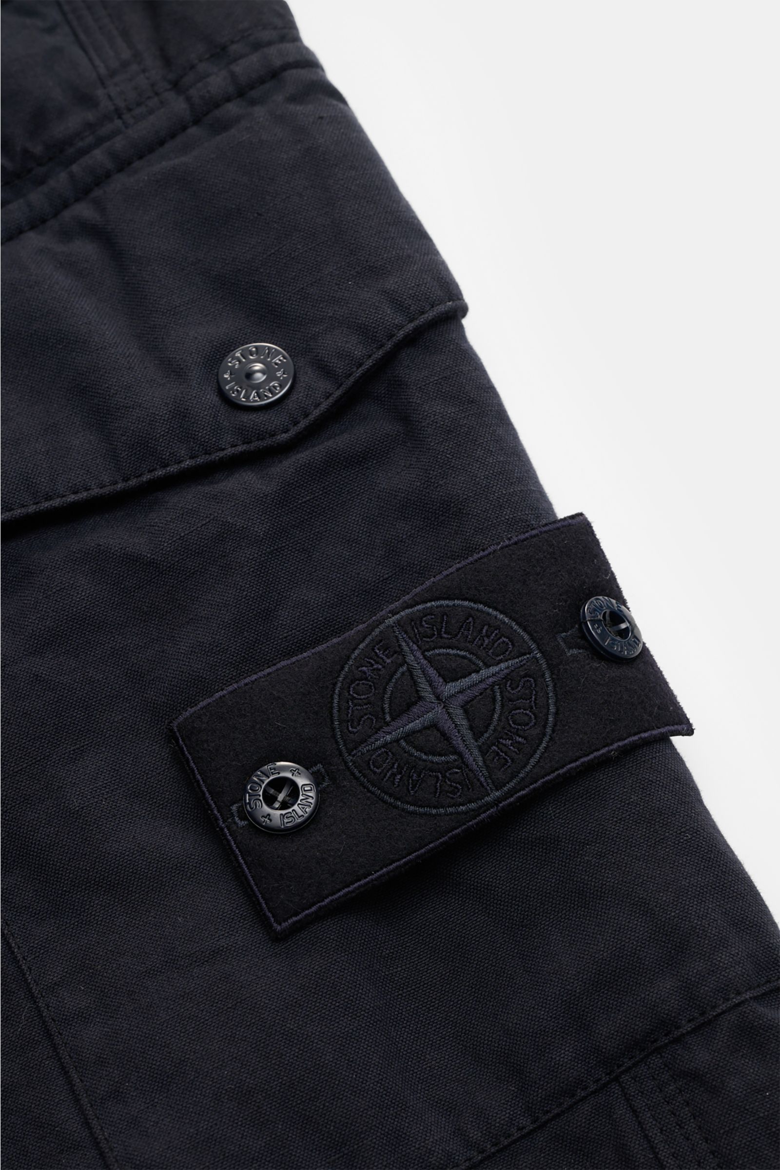 Stone Island Cargohose 'Ghost Piece' dark navy, Nahaufnahme seitlich auf Cargo-Tasche mit tonalem Kompass-Badge aus Baumwolle-Leinen-Mix.