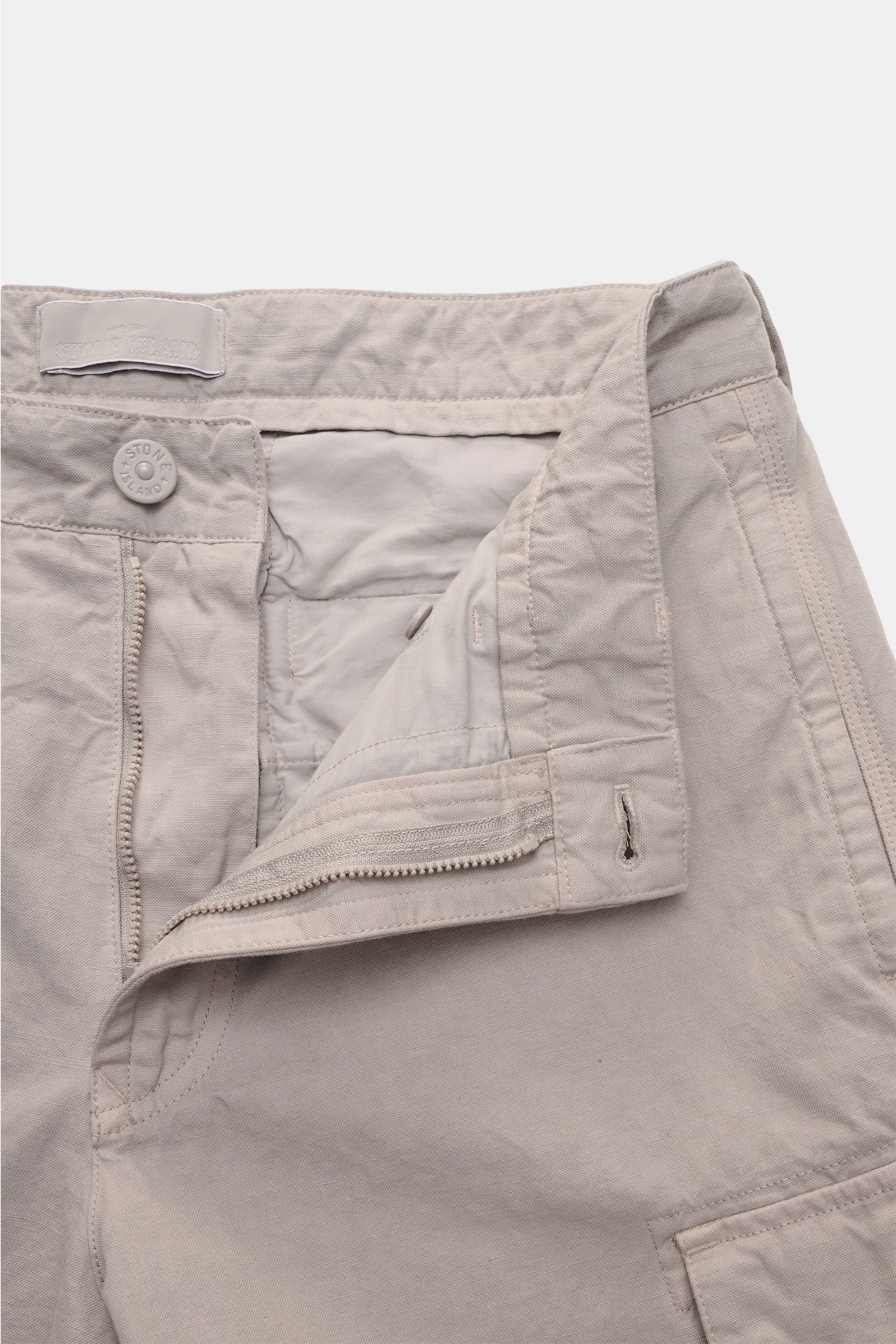 Stone Island Cargohose 'Ghost Piece' beige aus Baumwolle und Leinen, Regular Fit, offener Bund mit Knopf und Reißverschluss, seitliche Taschen, tonales Kompass-Badge, frontal fotografiert.