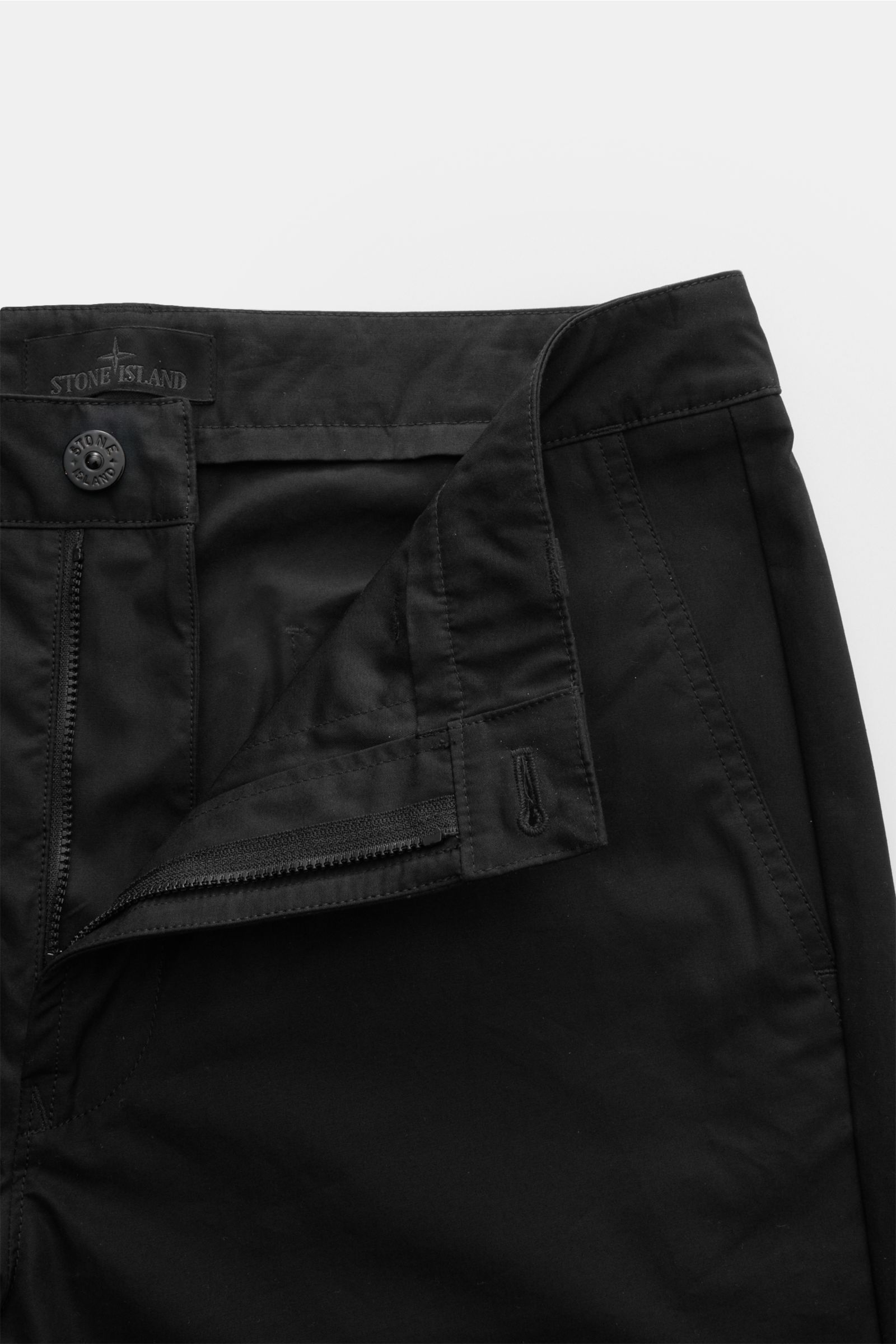 Stone Island Cargohose 'Ghost Piece' schwarz aus Baumwoll-Twill, knöchellang, Tapered Fit, frontal mit offenem Reißverschluss und Knopf.