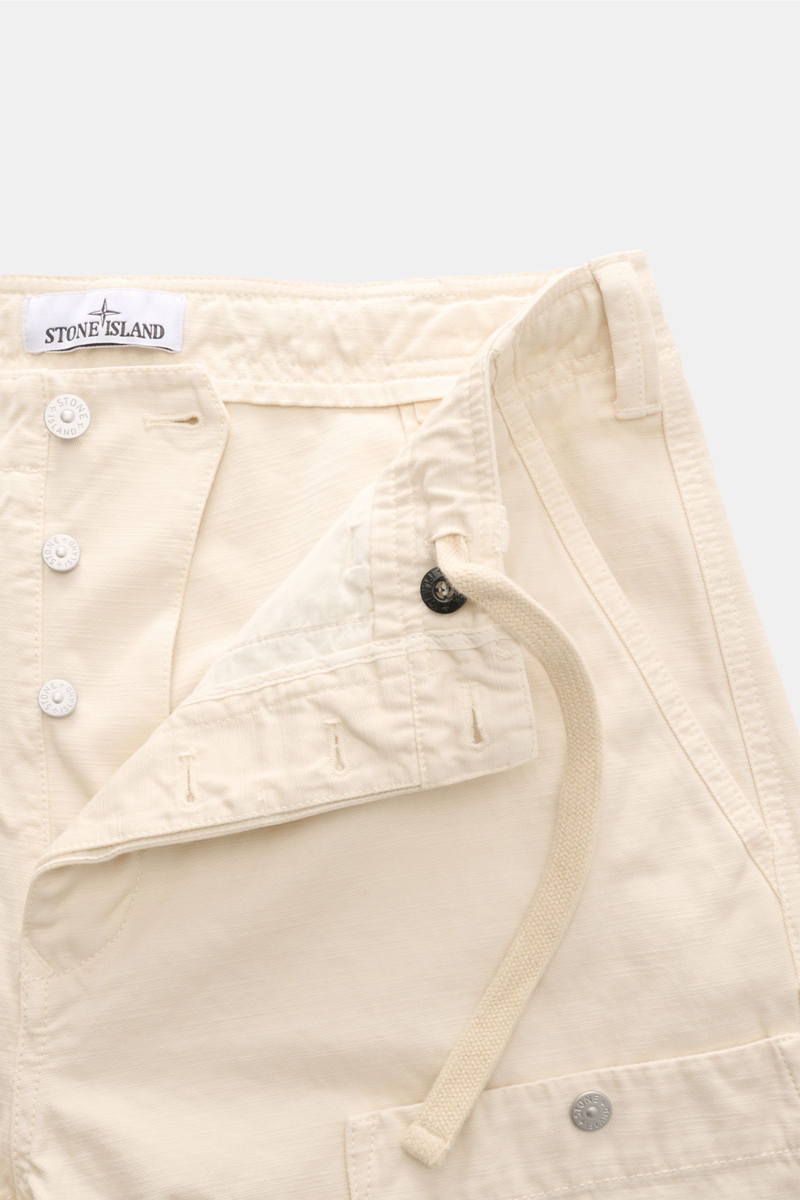 Stone Island Cargohose 'Marina' creme shown close-up from the front, highlighting button fly, inner drawstring, and fabric texture. Maritime Utility-Ästhetik: Die Cargohose aus der 'Marina'-Kollektion von STONE ISLAND vereint funktionale Details mit lässi