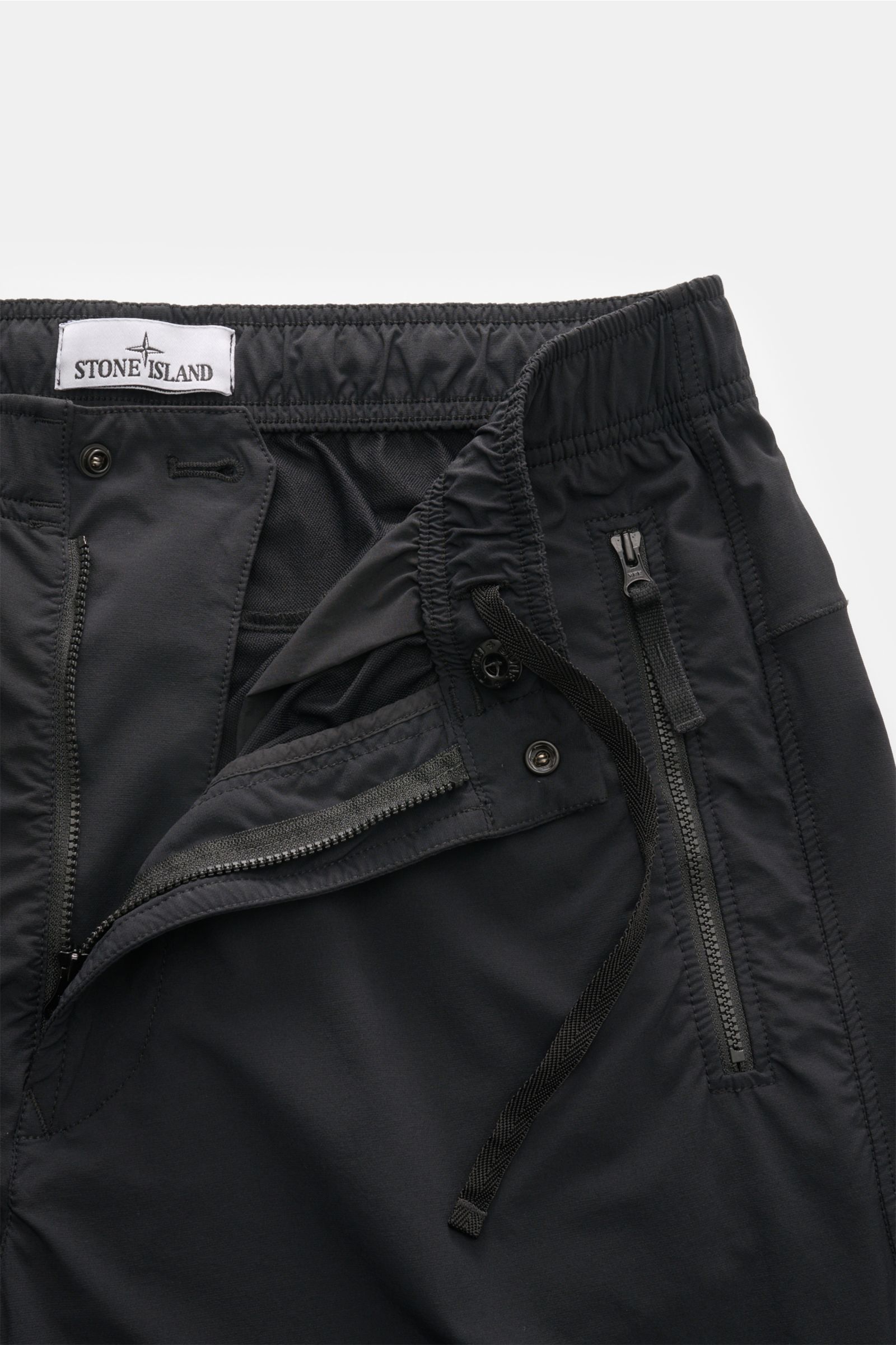 Stone Island Jogger pants black shown from a close-up front perspective with zipper, snap button, and drawstring, made of high-quality microfibre. Create casual looks for the spring season: These jogger pants by STONE ISLAND are synonymous with sporty and