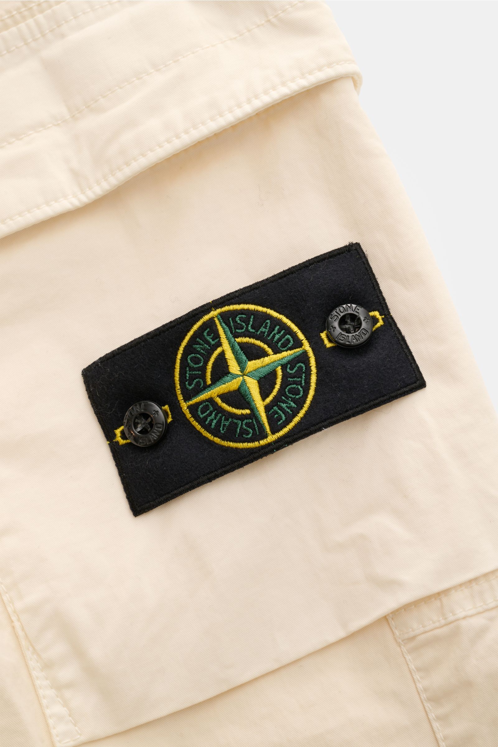 Stone Island Cargo-Jogpants 'Regular Tapered' creme, Detailaufnahme des Kompass-Badges auf klassischer Cargo-Tasche aus Bio-Baumwolle.