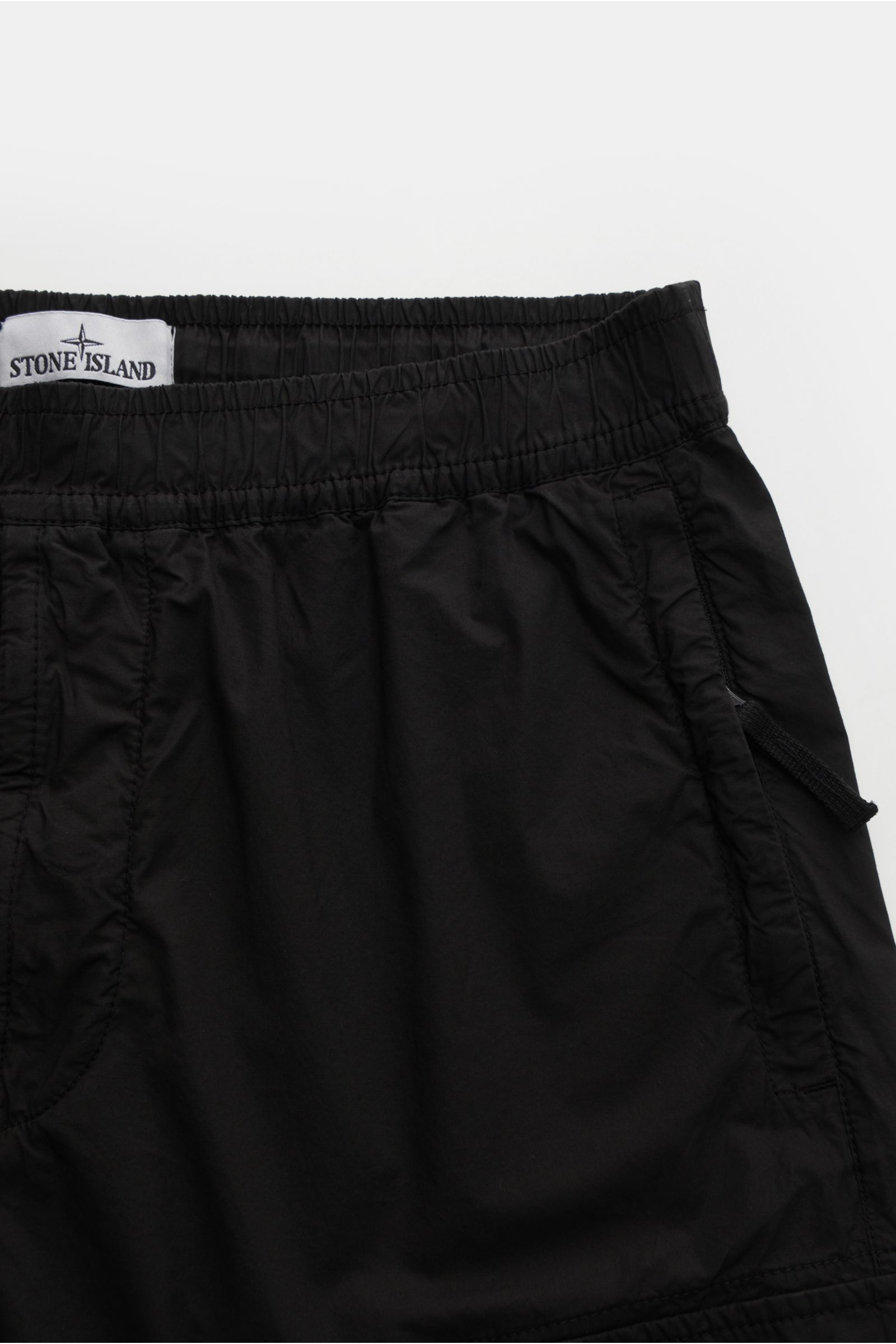 Close-up top view of Stone Island Cargo-Jogpants 'Regular Tapered' schwarz in black cotton with elastic waistband, side seam pockets, and compass badge, showing soft fabric and utility-inspired details for urban everyday wear. Für alle, die Funktion un
