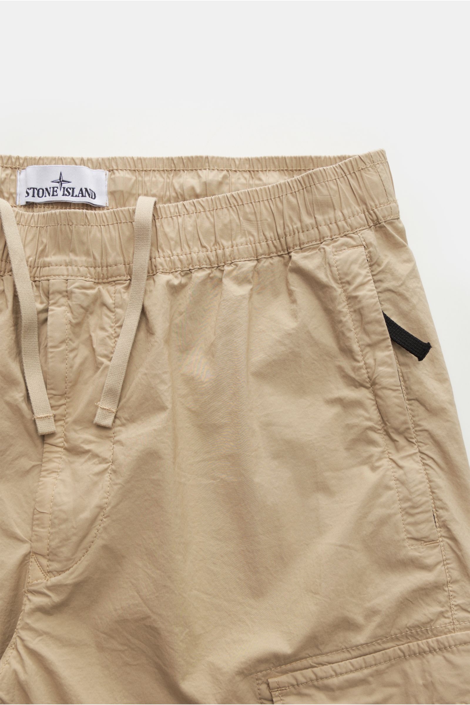 Stone Island Cargo-Jogpants 'Regular Tapered' beige shown from a front close-up perspective, highlighting elastic cotton waistband with drawstring, side zippered pockets, classic cargo pockets, knee darts, back pocket with snap button, elastic cuffs, and 