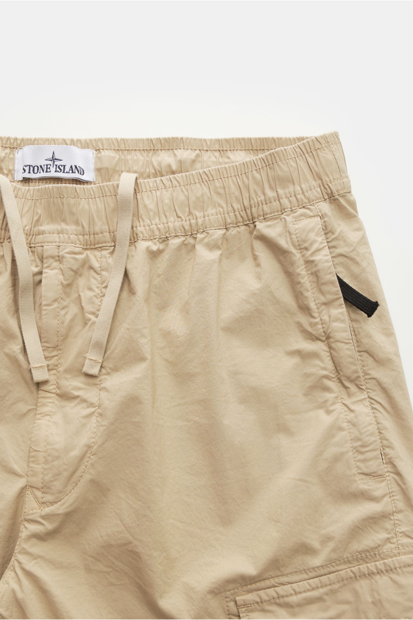 Beige Stone Island Cargo-Jogpants 'Regular Tapered' aus elastischer Baumwolle, mit Tunnelzug, Reißverschluss, Taschen und Kompass-Badge, Nahaufnahme frontal.