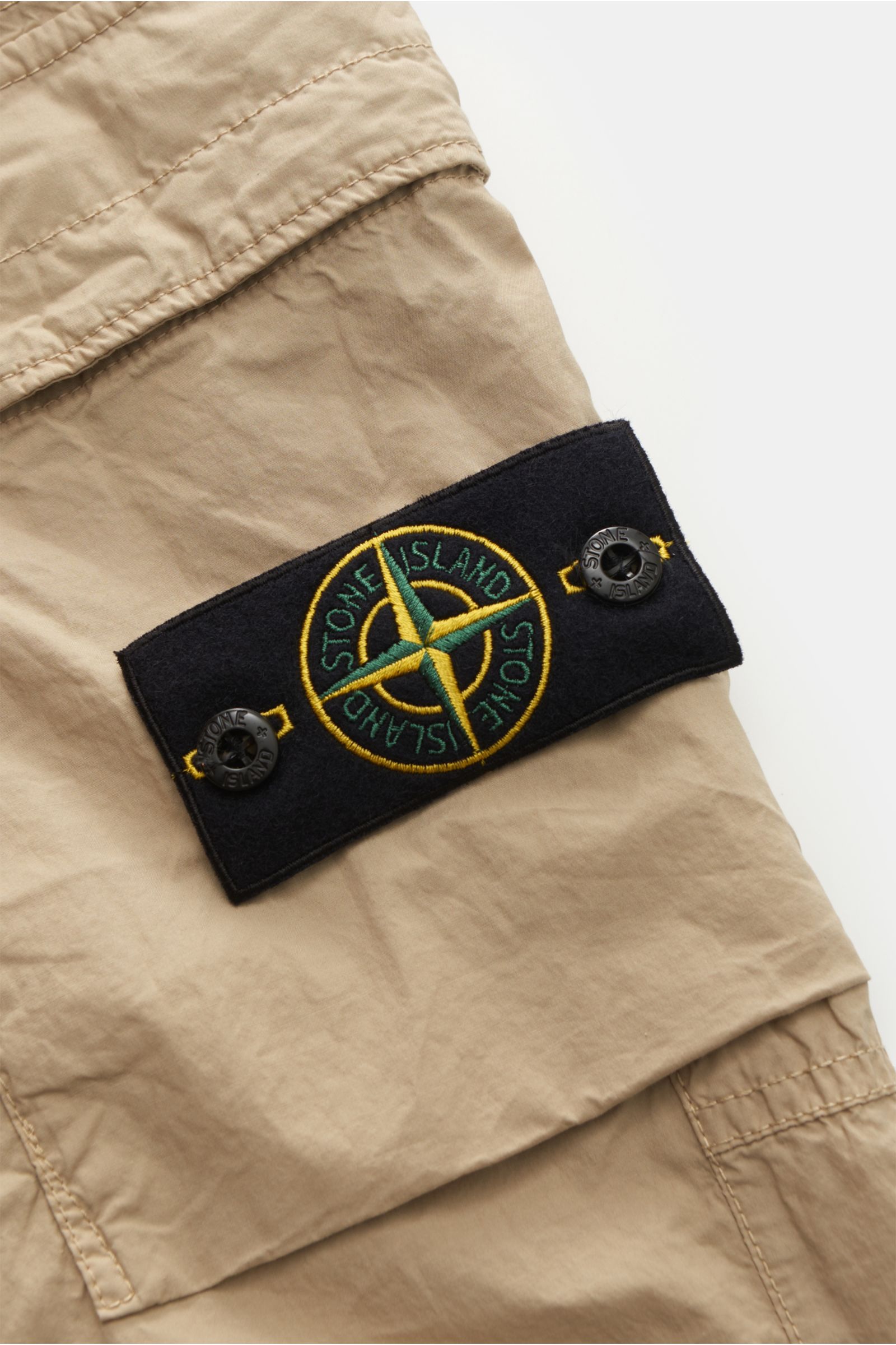 Stone Island Cargo-Jogpants 'Regular Tapered' beige close-up from above showing black compass badge on soft, elastic cotton fabric with utility-inspired details. Für alle, die Funktion und Stil vereinen wollen – diese Cargo-Jogpants von STONE ISLAND is