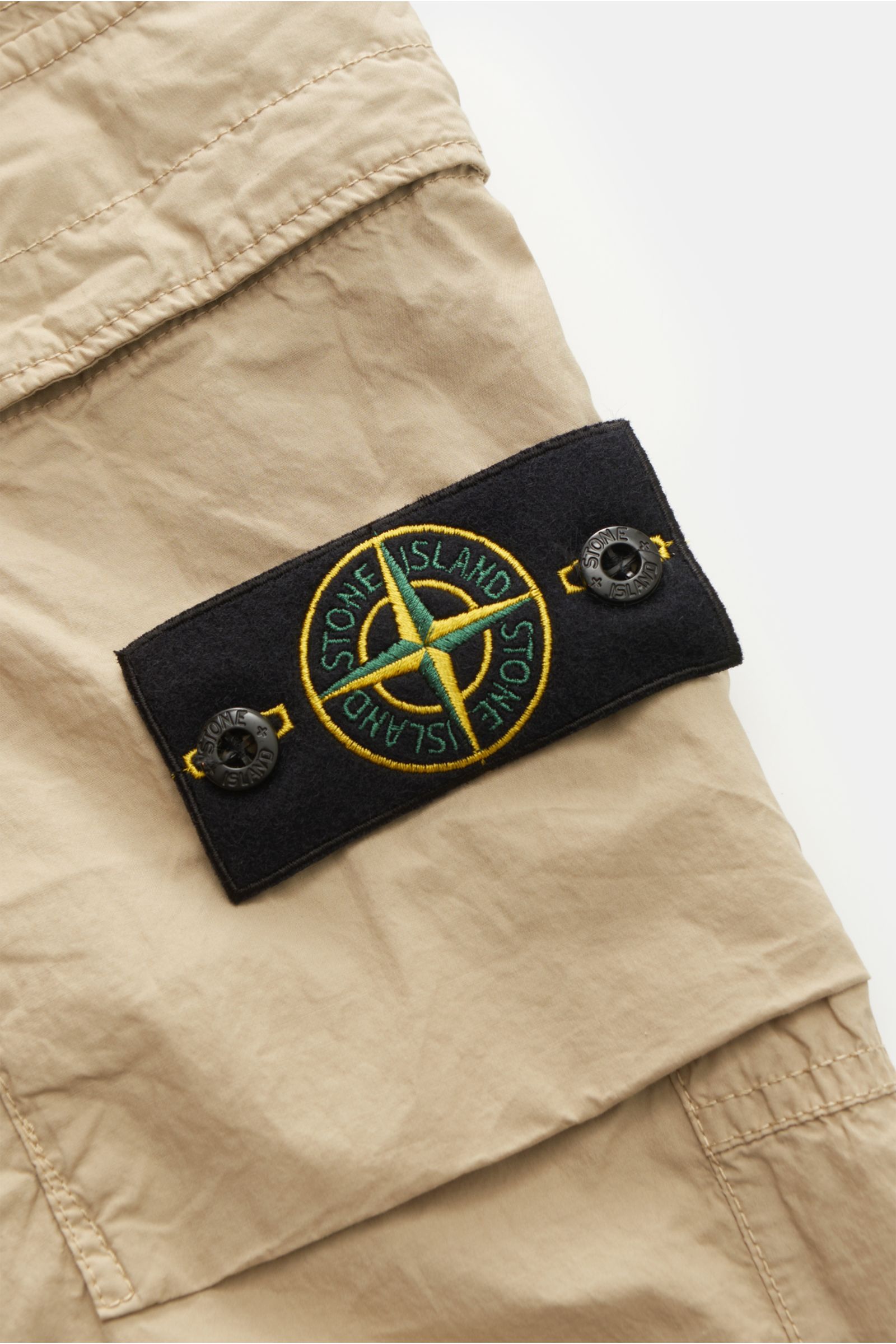 Nahaufnahme der Stone Island Cargo-Jogpants 'Regular Tapered' beige, Fokus auf klassisches Kompass-Badge und Baumwollstoff.