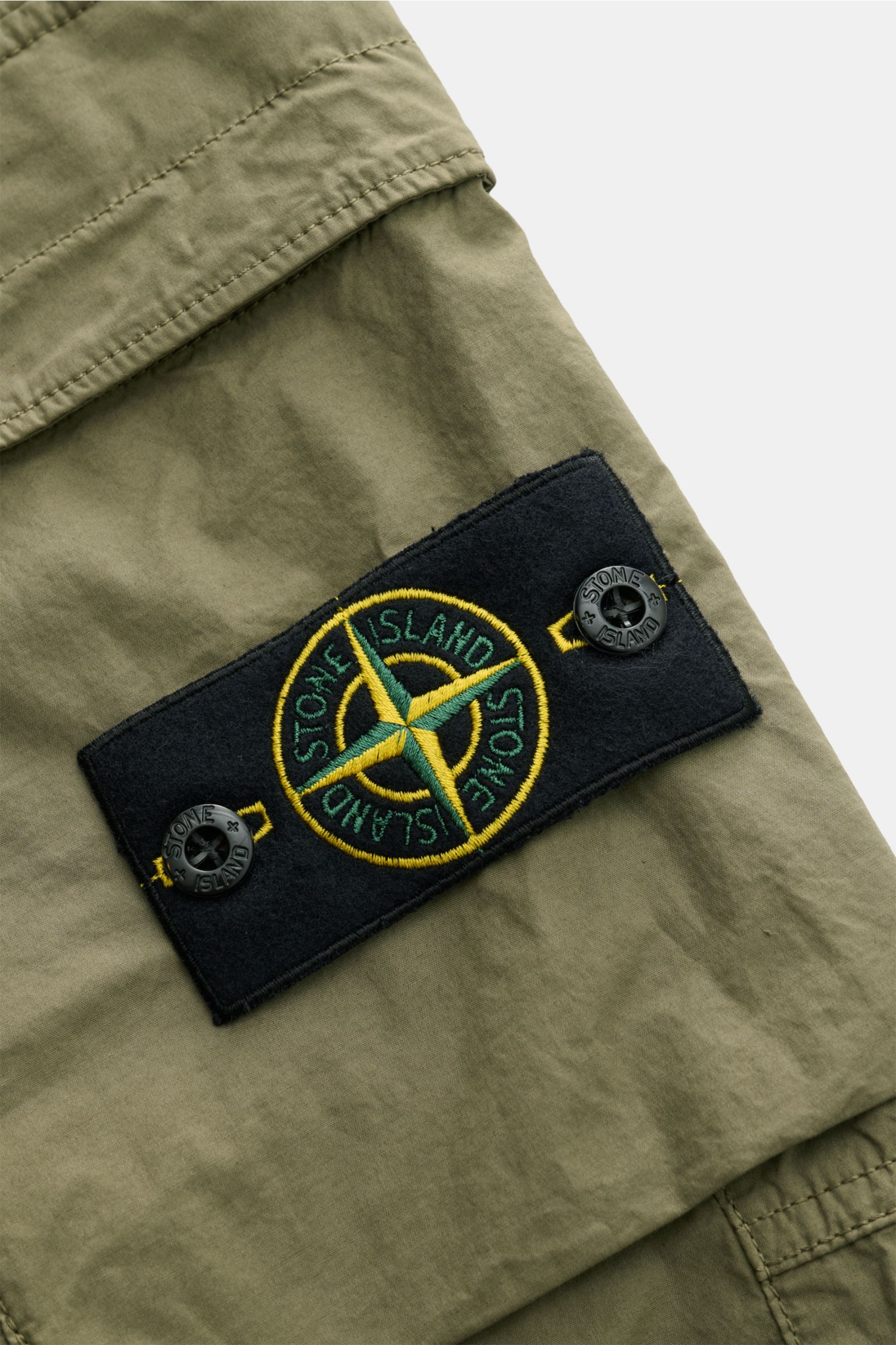 Nahaufnahme der Stone Island Cargo-Jogpants 'Regular Tapered' oliv, Fokus auf das klassische Kompass-Badge aus Baumwolle mit weichem Griff.