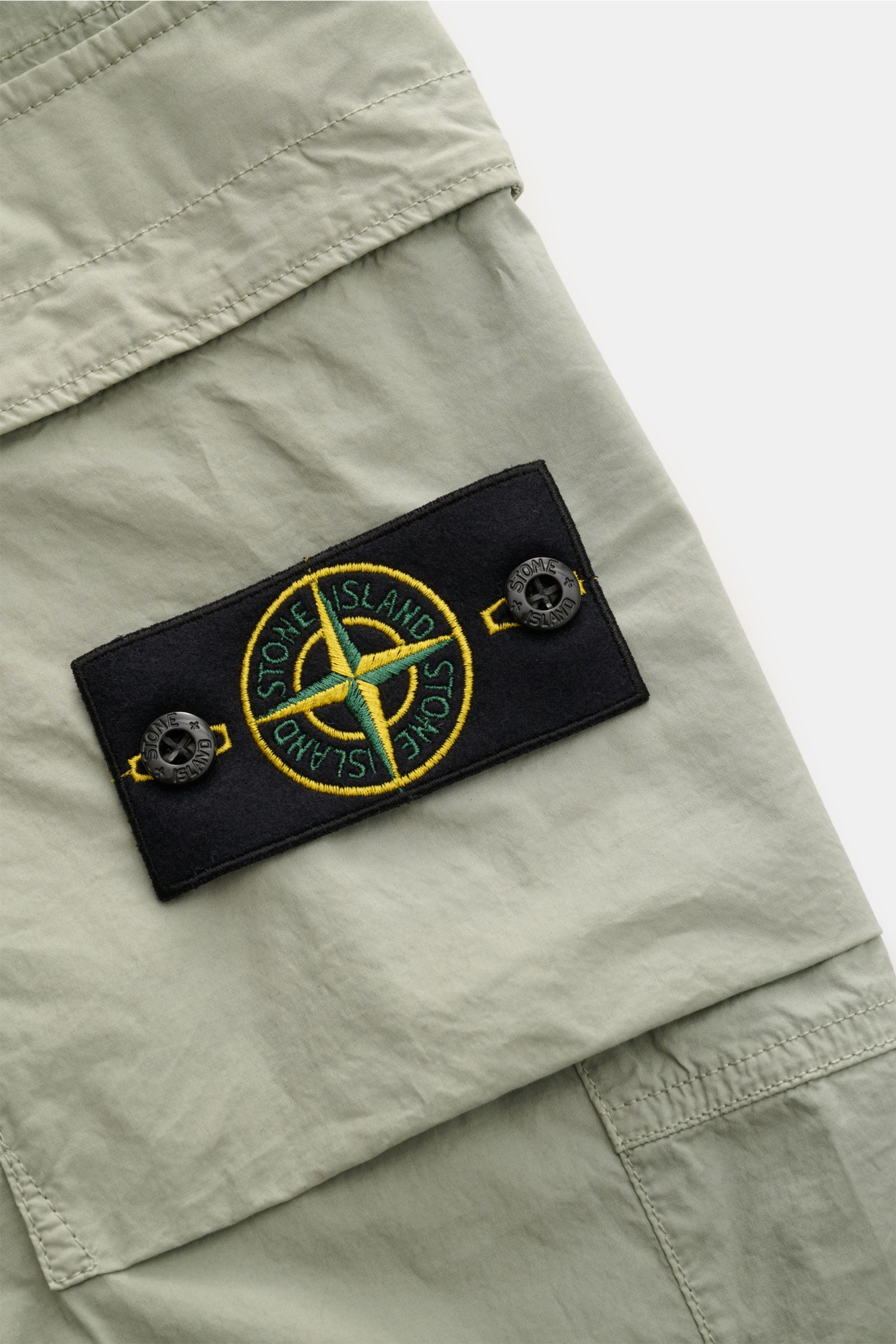 Nahaufnahme der Stone Island Cargo-Jogpants 'Regular Tapered' salbei, elastische Baumwolle, Cargo-Tasche mit Kompass-Badge.