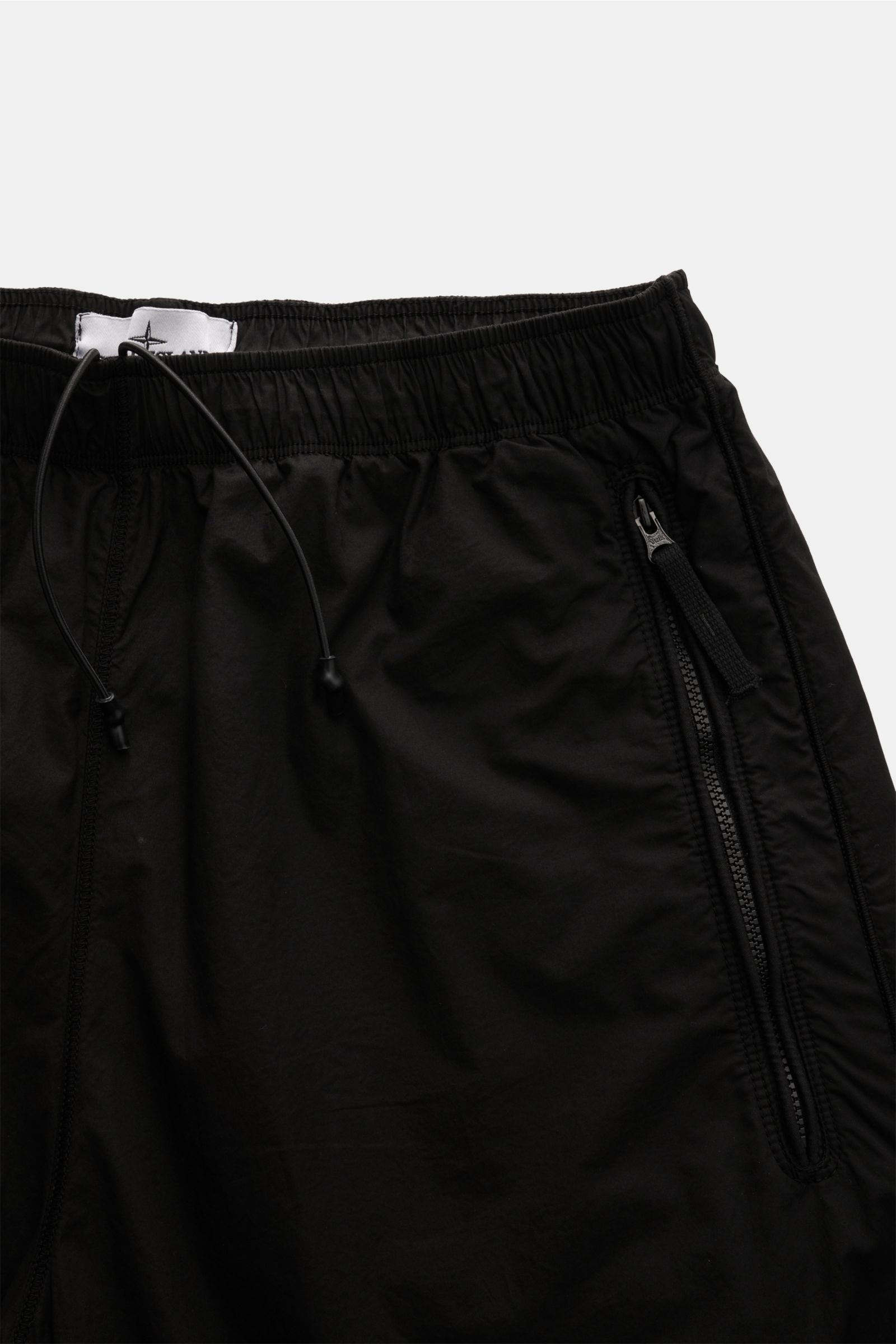 Stone Island Jogpants schwarz in Nahaufnahme von oben, elastische Baumwolle, Zipper-Taschen, elastischer Bund mit Tunnelzug.