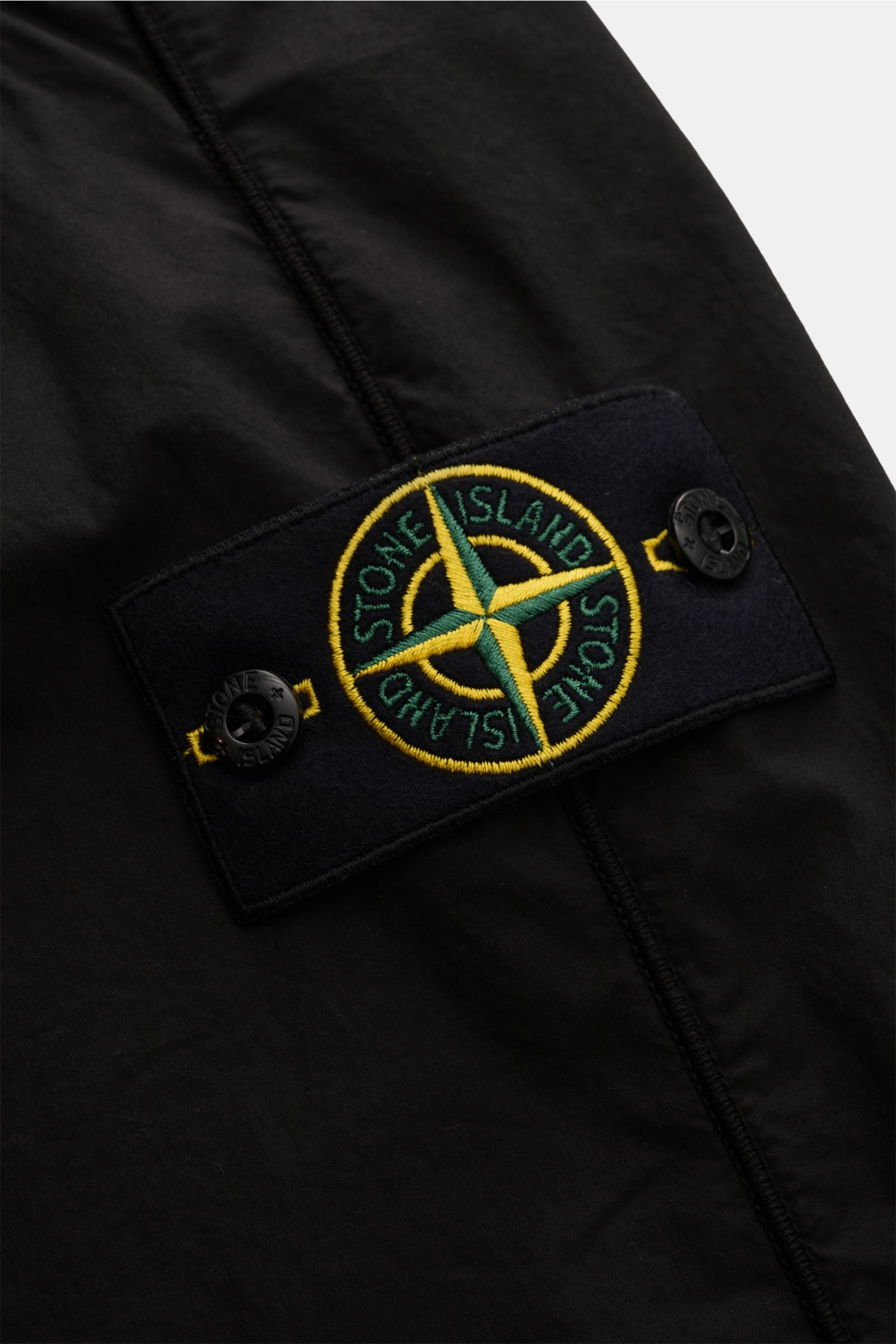 Stone Island Jogpants schwarz, Detailansicht des Kompass-Badges an elastischer Baumwoll-Jogpant mit Rippstrick-Einsatz.