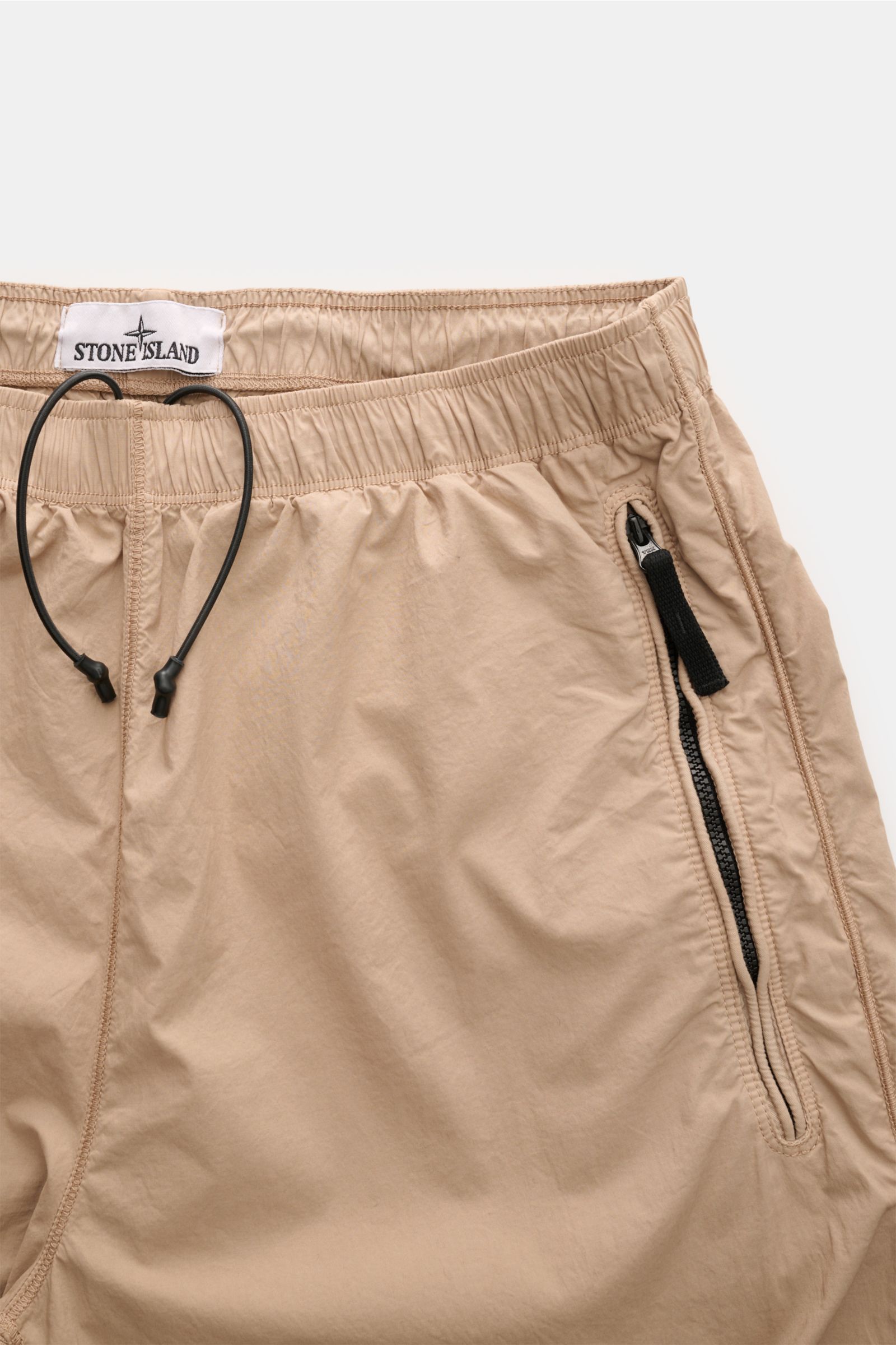 Stone Island Jogpants sand, Nahaufnahme von oben, elastische Baumwolle, elastischer Bund mit Tunnelzug, Zipper-Tasche, labeltypisches Kompass-Badge.