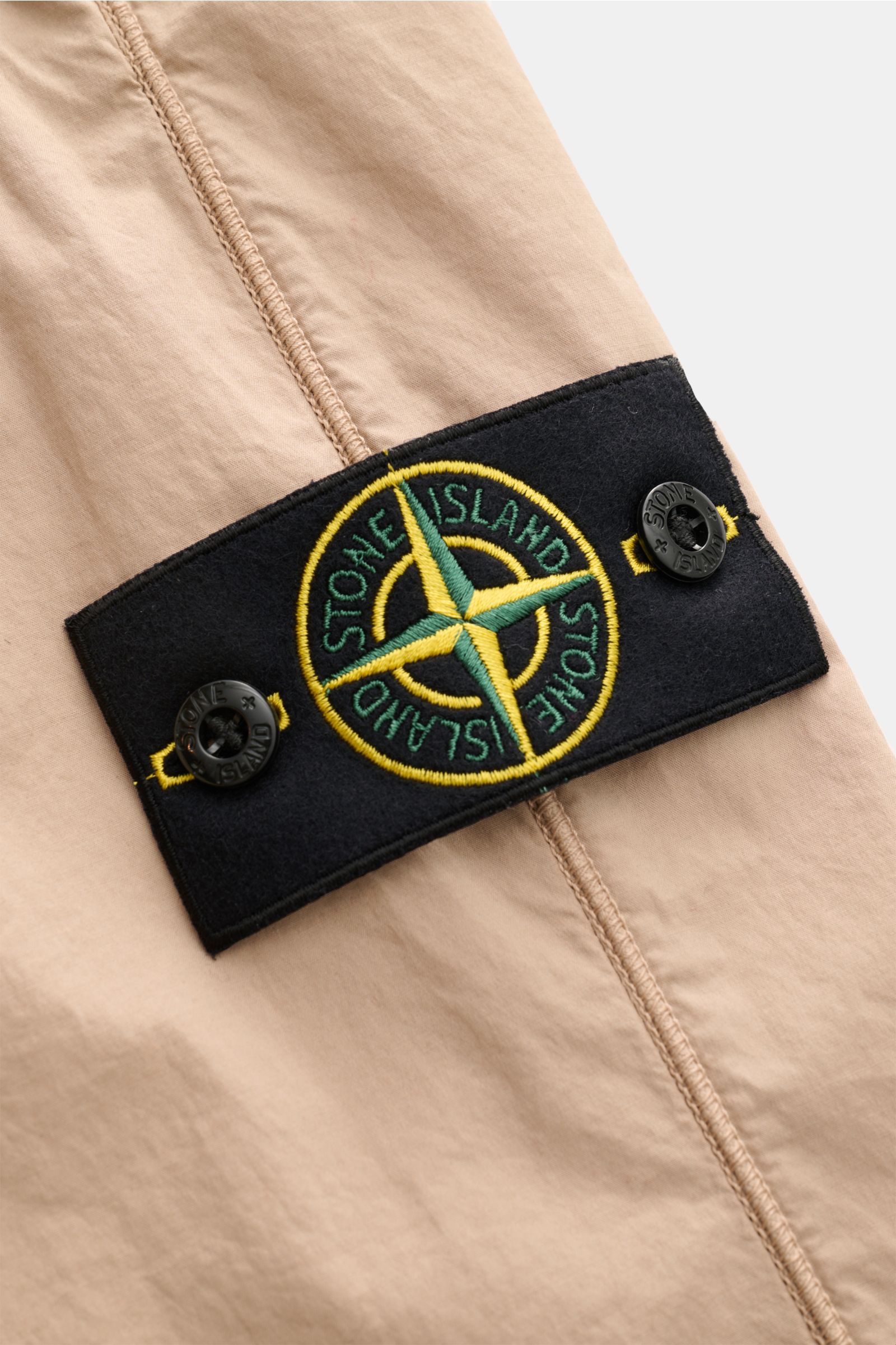 Alt-Tag (124 Zeichen): Nahaufnahme der Stone Island Jogpants sand mit Label-Kompass-Badge, elastischer Baumwolle und glattem Griff, seitliche Naht sichtbar.