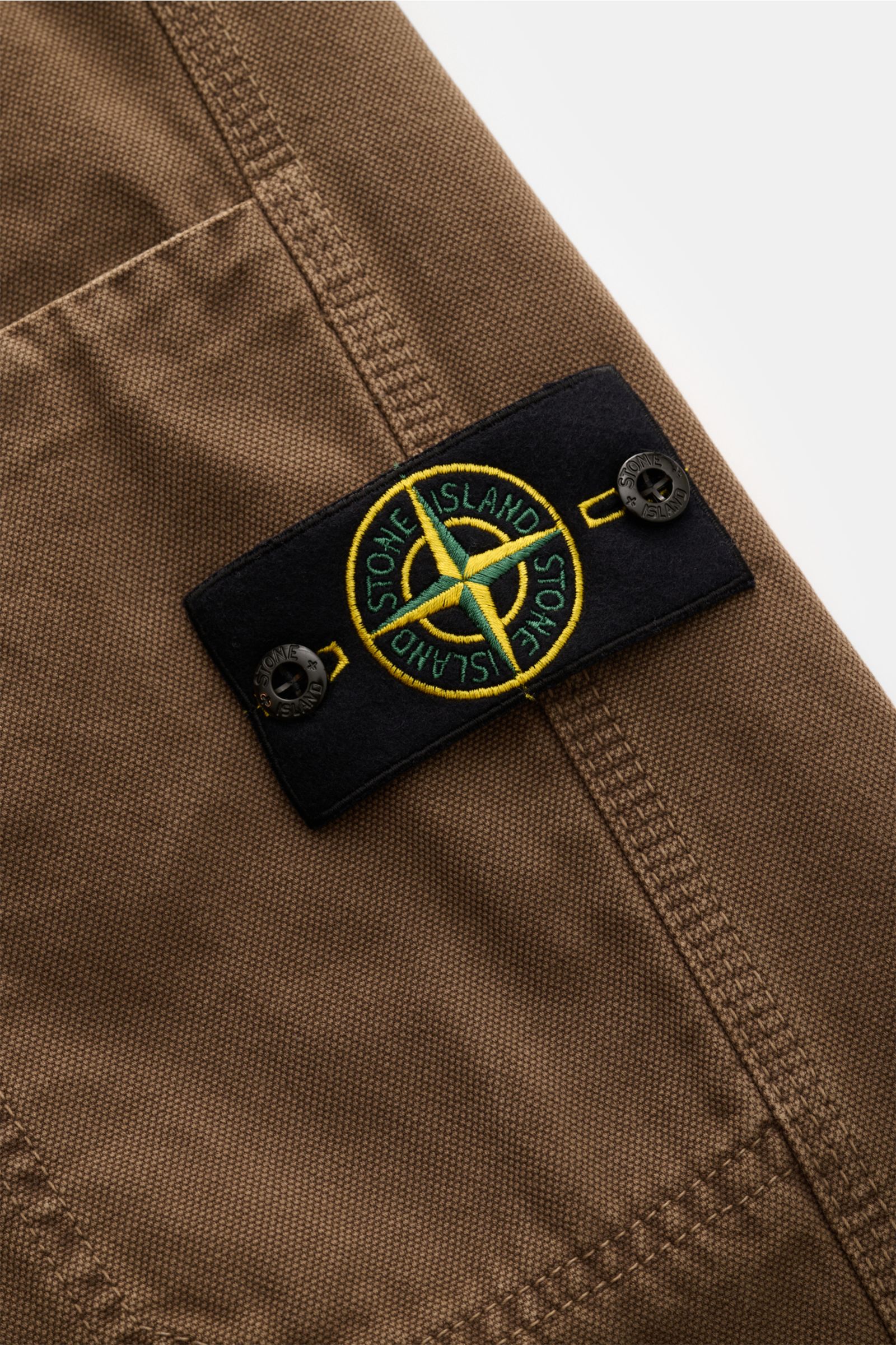 Nahaufnahme der Stone Island Cargo-Jogpants 'Panama' khaki mit dem typischen Kompass-Badge auf griffiger, stückgefärbter Bio-Baumwolle.