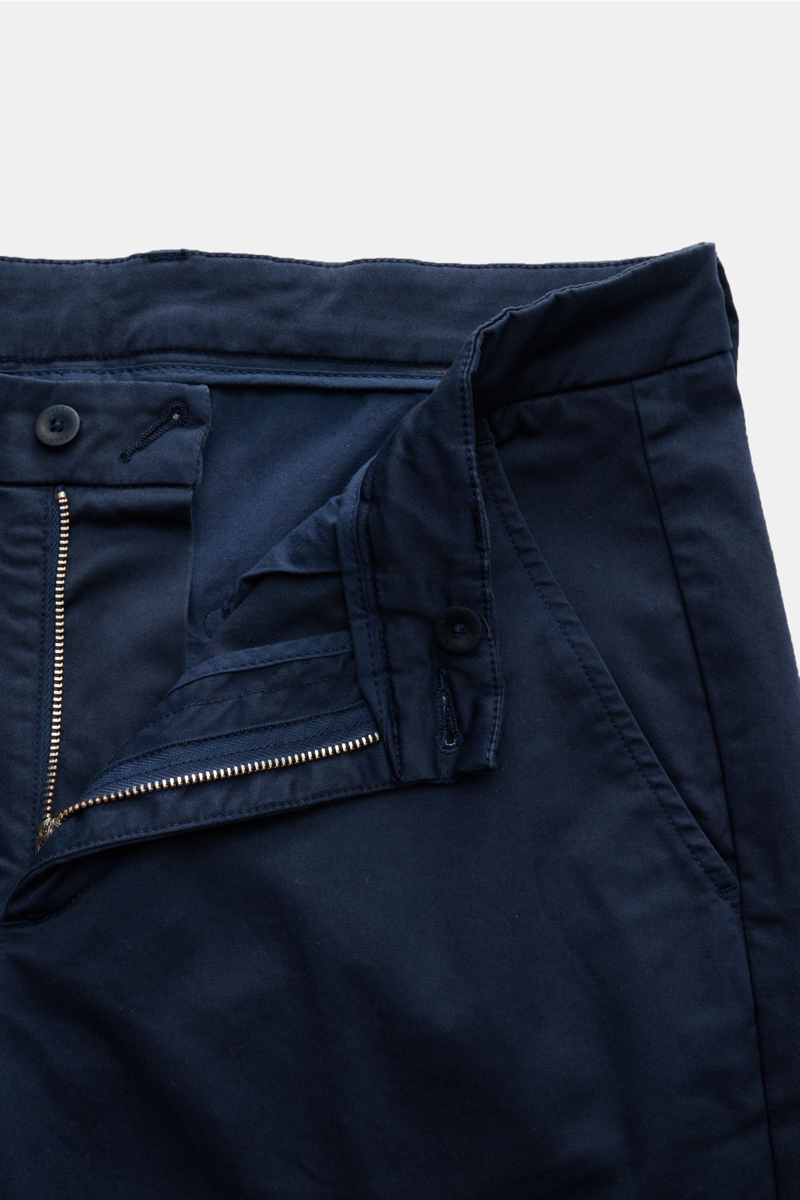 Auf dem Bild ist die Hose 04651/ A trip in a bag Chino navy aus Twill Baumwolle mit Reißverschluss, Bundknopf, französischen Taschen aus schräger Nahaufnahme zu sehen. Leicht elastisch, leicht griffig, tapered fit, reguläre Oberschenkelweite, knöchellang,