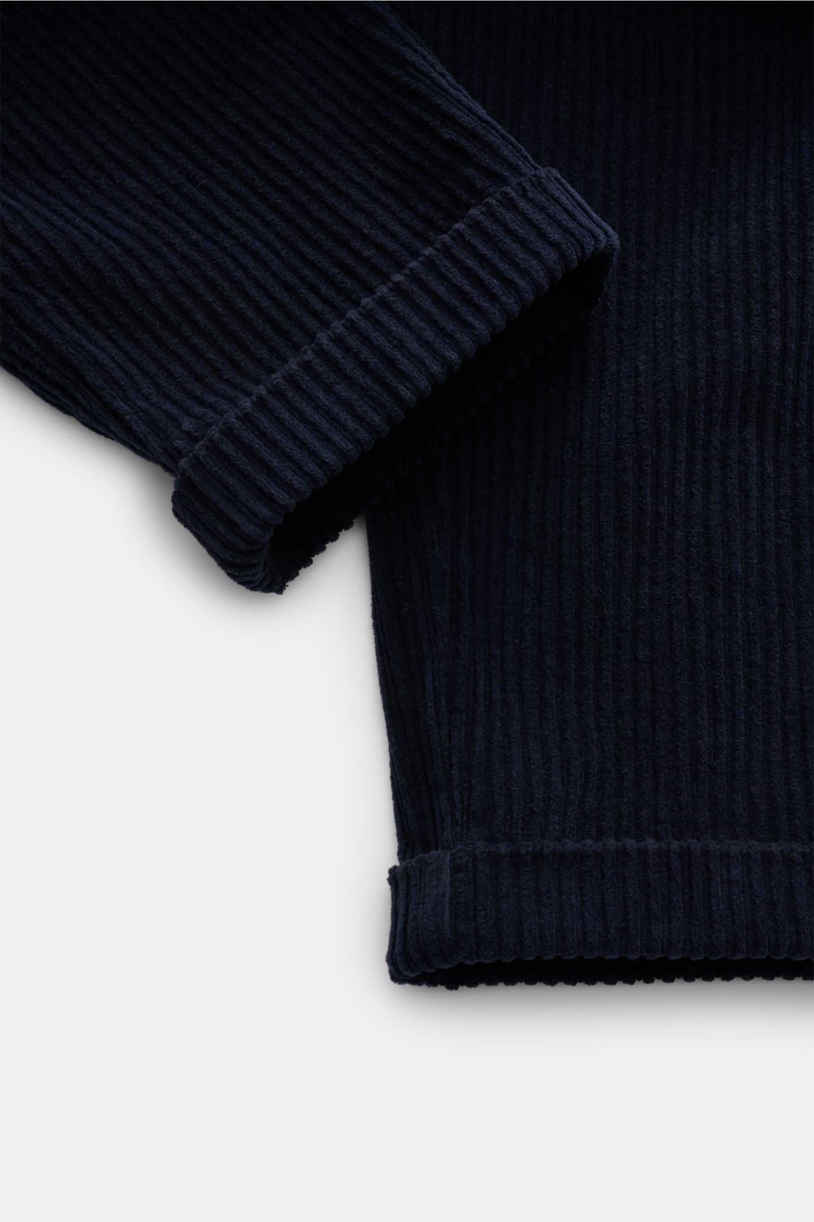 Close-up image from a top-front angle of the cuffed hem of 04651/ A trip in a bag Corduroy cargo pants navy, showing wide wale corduroy made of cotton with slight stretch content and a soft feel. The pants feature a tapered fit with regular thigh width, a