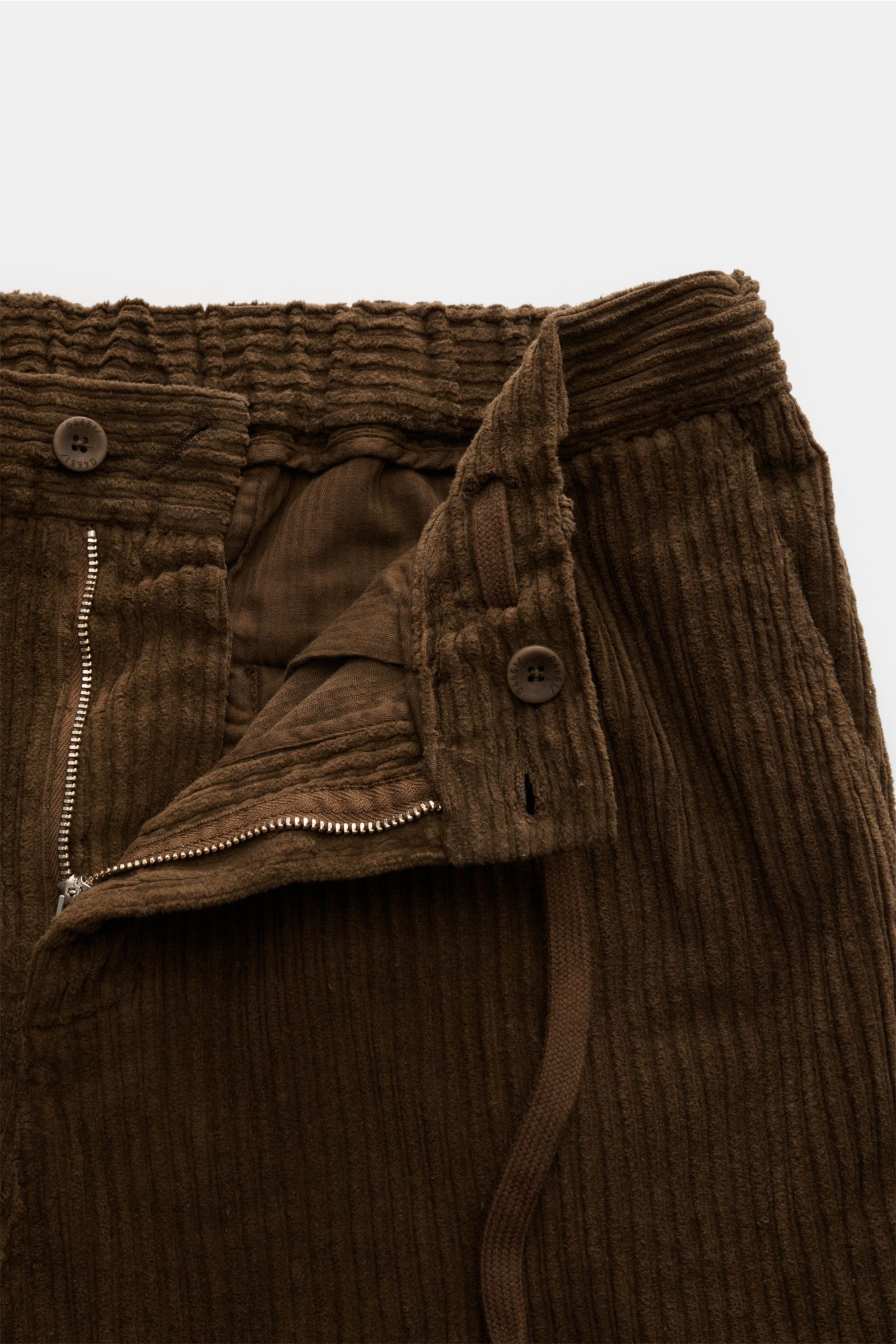Close-up front view of 04651/ A trip in a bag Corduroy cargo pants brown showing wide wale cotton corduroy, slight stretch, soft feel, zip and waist button, partially elasticated waistband with drawstring, and signature cargo pockets.