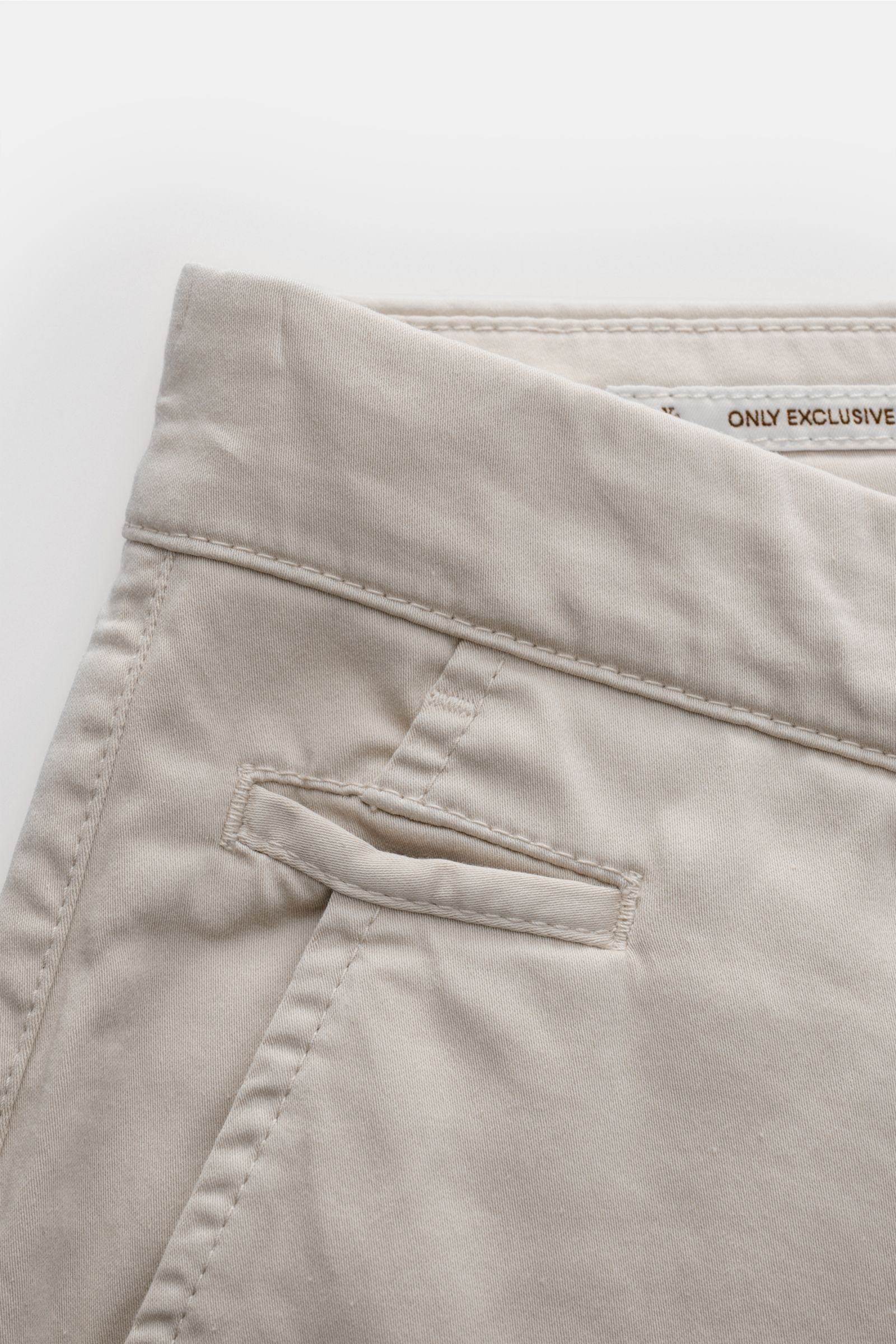 Nahaufnahme der oberen linken Seite der Jacob Cohen Chino 'Bobby' beige aus feinem, elastischem Baumwoll-Twill mit schmal zulaufendem Slim Fit, französischer Tasche und paspelierter Münztasche, fotografiert von oben.