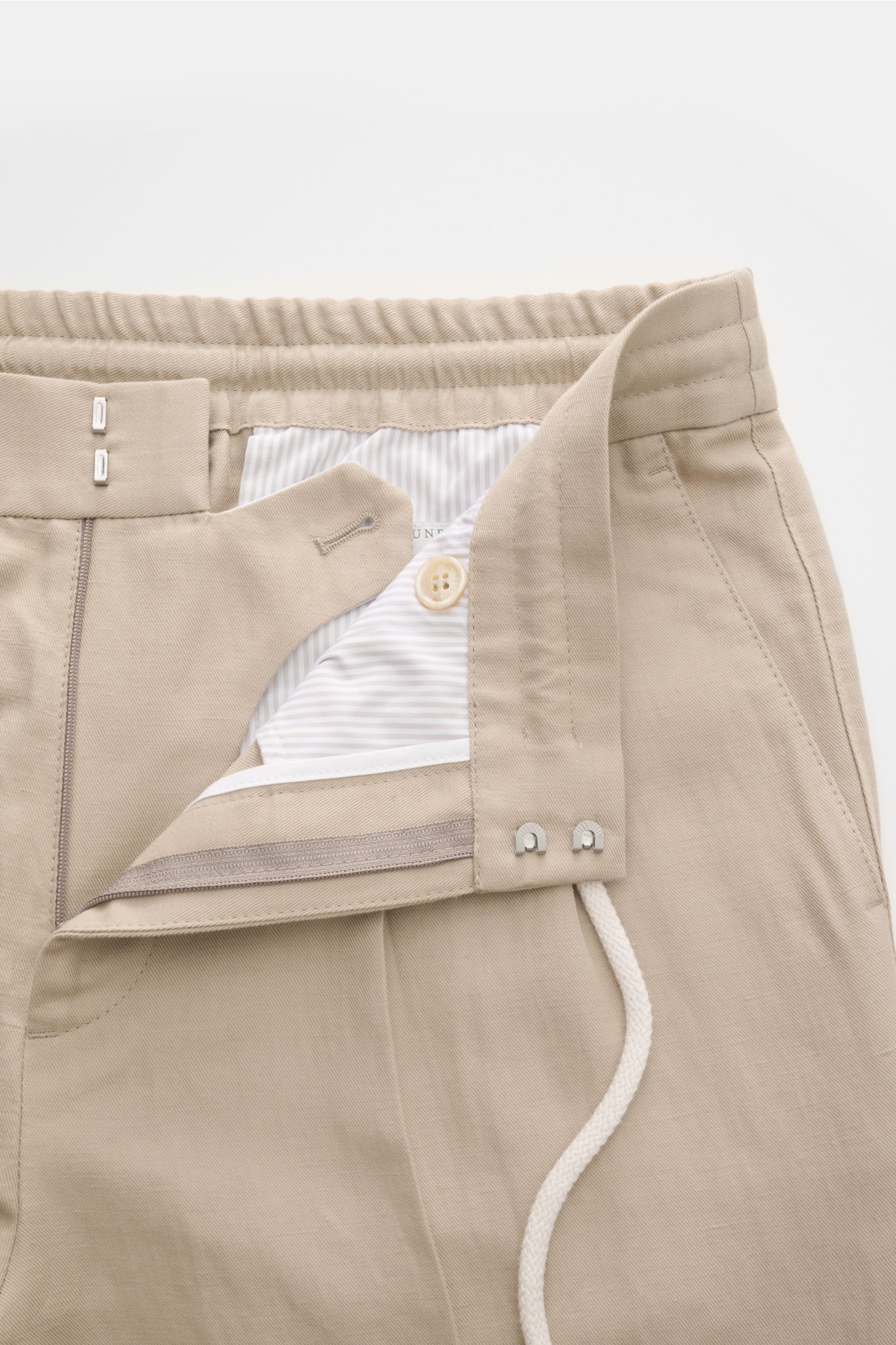 Beige Brunello Cucinelli Jogpants 'Leisure Fit' shown from a close-up front perspective, featuring a twill linen-cotton blend, elastic waistband with drawstring, zipper, hook closure, and detailed pocket stitching. Stil trifft Tragekomfort: Die Jogpant