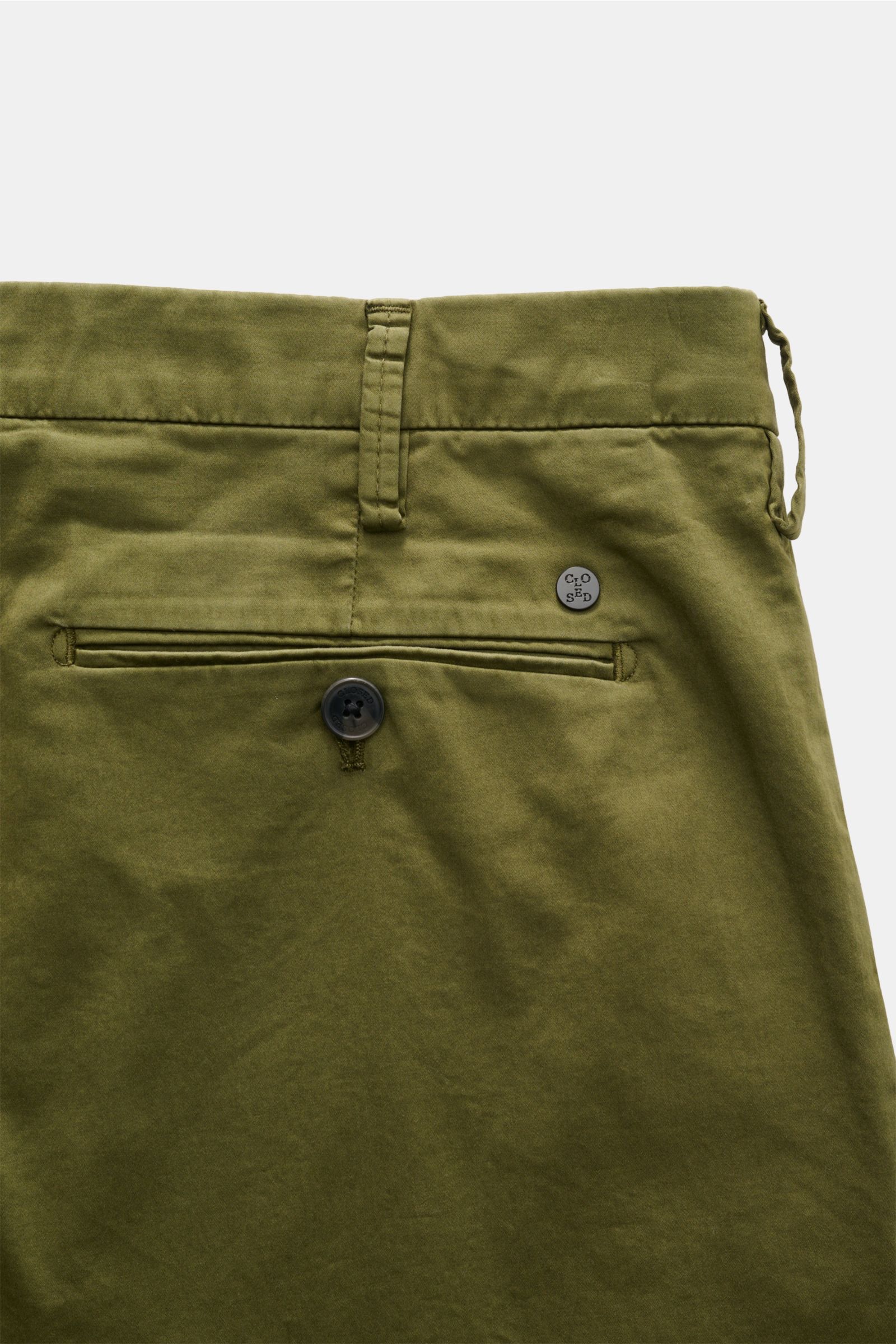 Detailaufnahme der Rückseite der Closed Baumwollhose 'Bergen Tapered' oliv mit paspelierter Gesäßtasche, Knopf und Metall-Initial, fotografiert von oben.