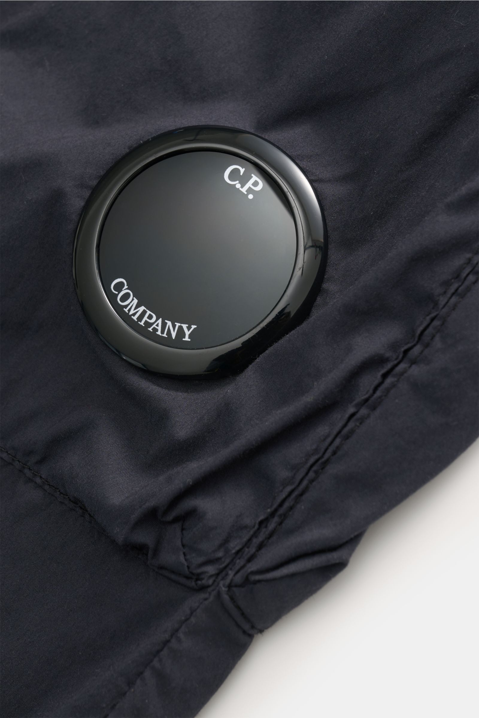 Nahaufnahme des labeltypischen Linsendetails an der C.P. Company Cargohose navy aus Baumwoll-Microfaser-Mix mit weichem Griff.