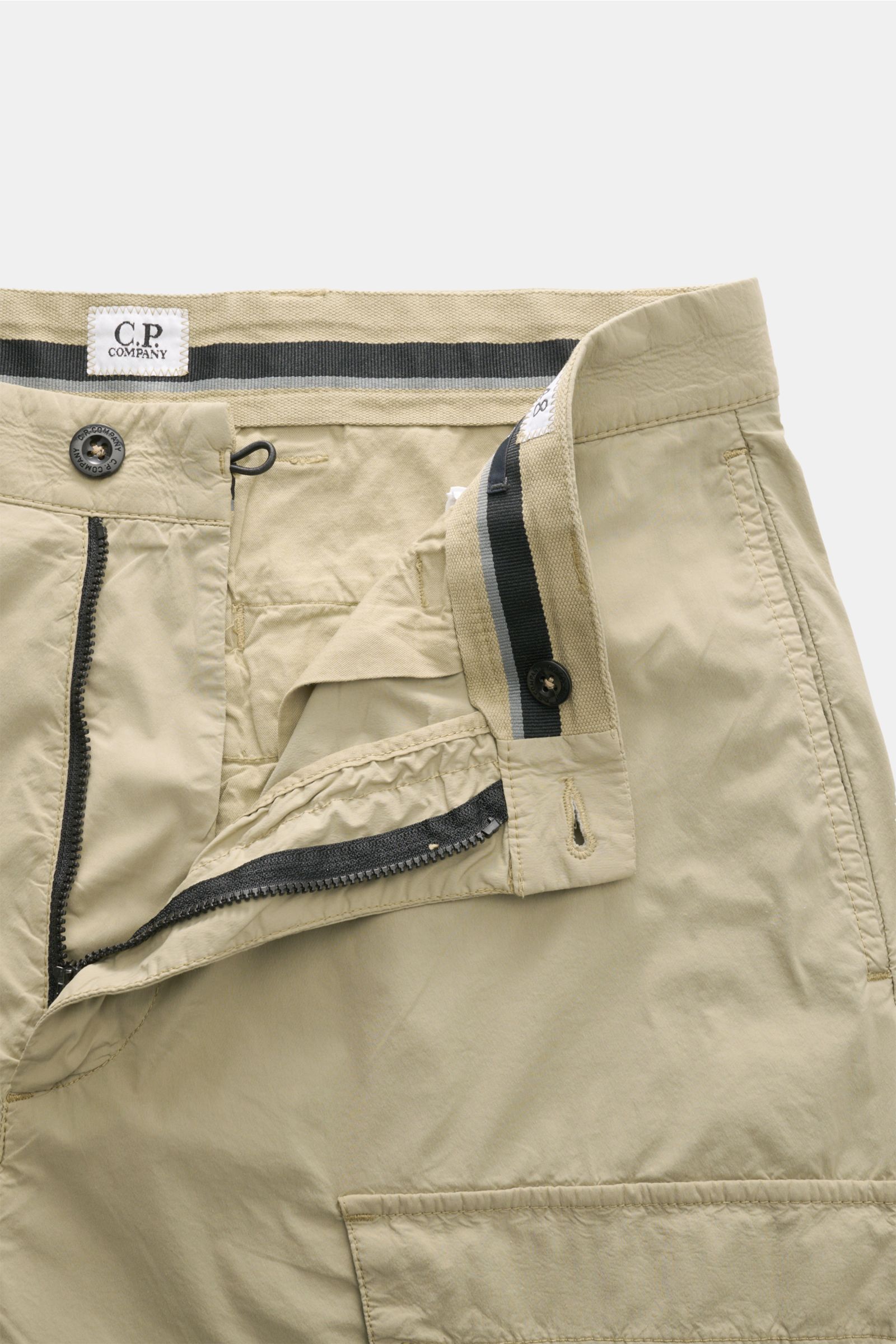 C.P. Company Cargohose sand in Nahaufnahme von vorne, Baumwoll-Microfaser, Tapered Fit, Cargo- und Gesäßtaschen, Reißverschluss, Bundknopf.