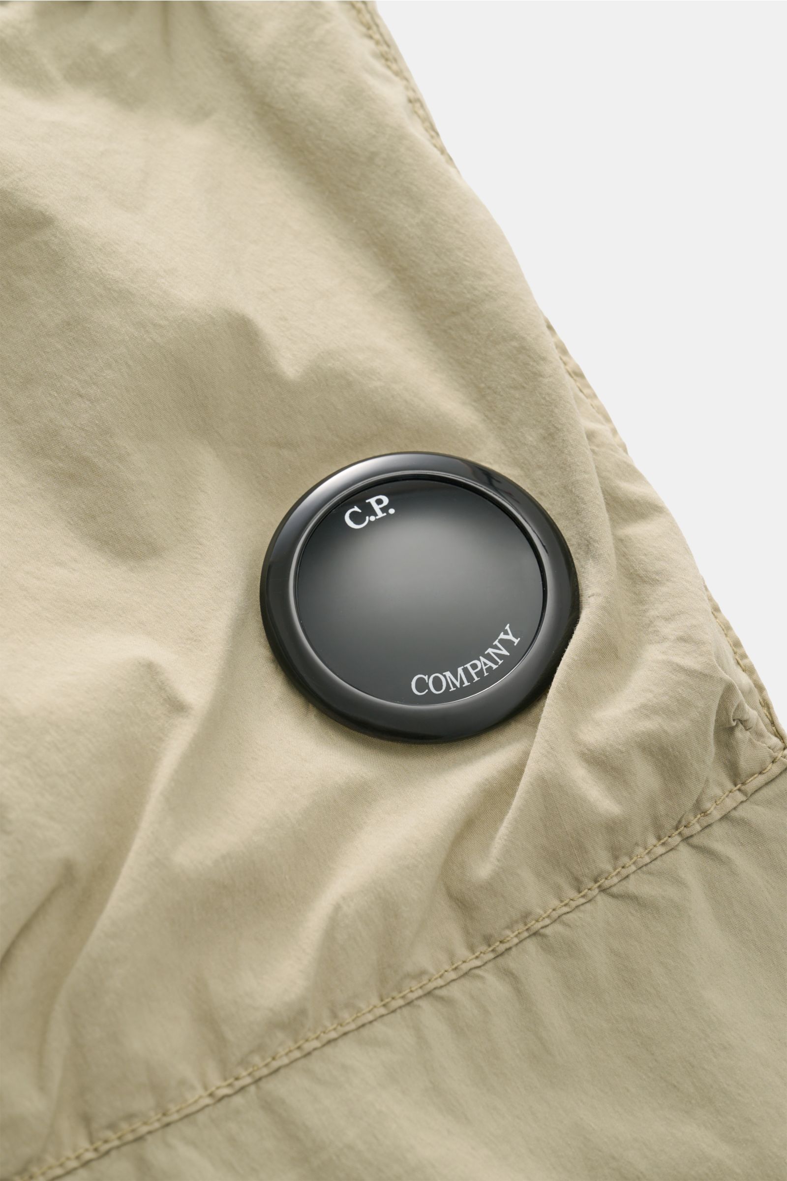 Nahaufnahme der labeltypischen Linse auf der C.P. Company Cargohose sand aus Baumwoll-Microfaser-Mix mit weichem Griff.