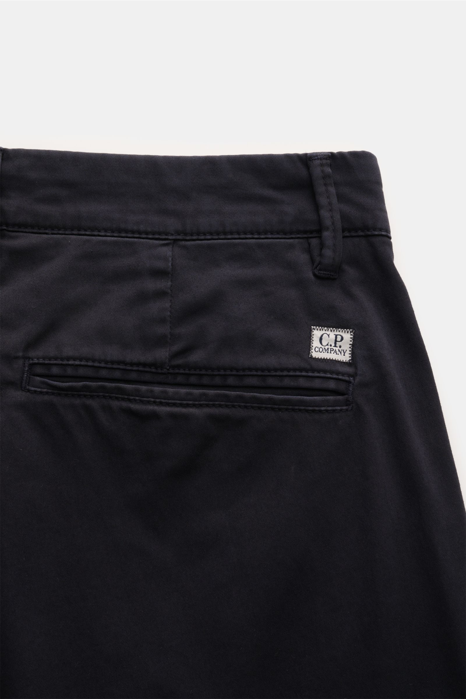 C.P. Company Cargohose dark navy close-up rear view showing gusset waistband, welt pocket with C.P. Company label, gabardine cotton fabric, comfortable stretch, soft touch, regular fit, tapered leg, zipper and button closure, side seam and practical cargo
